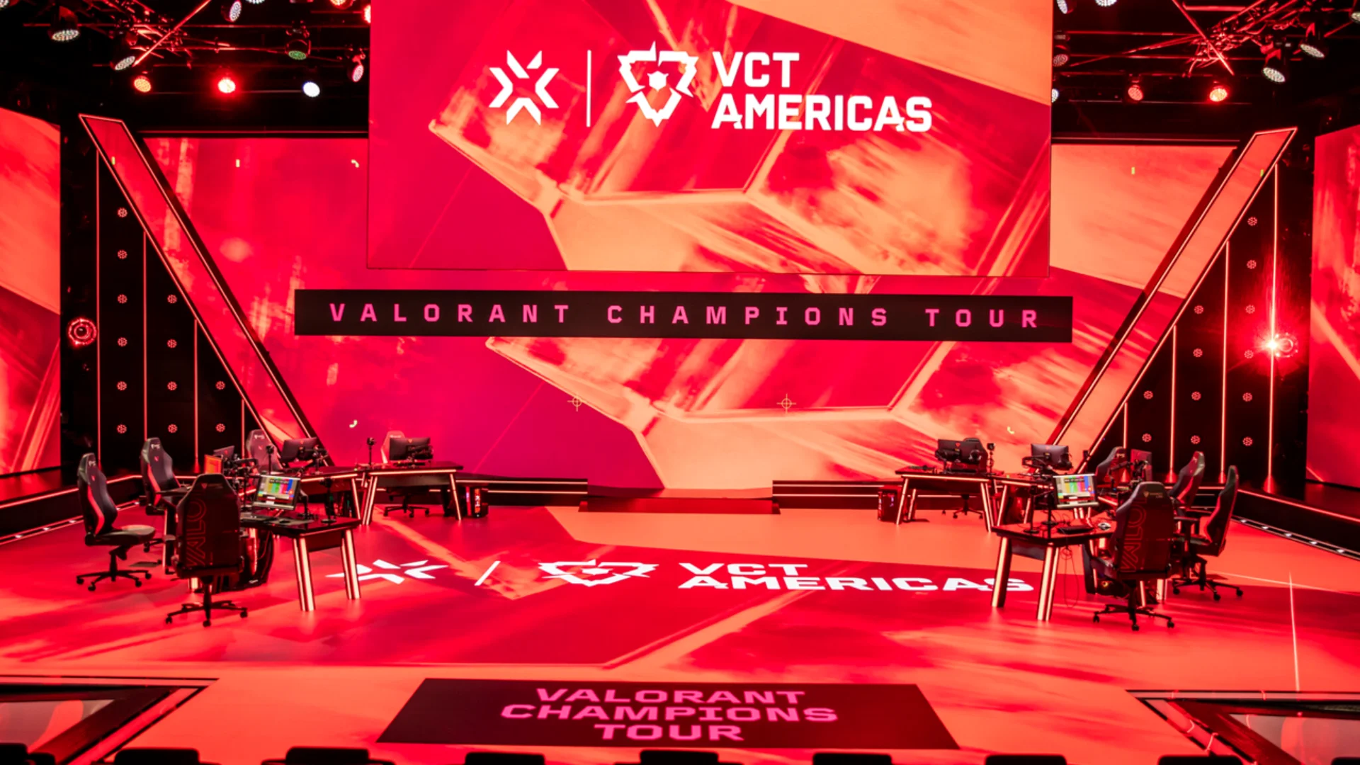 VALORANT Champions Tour Americas stage with red lighting, gaming desks and team stations prepared for competition.