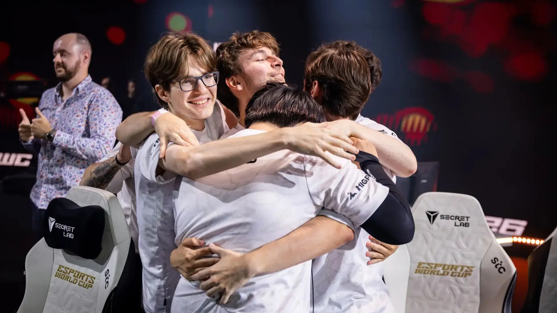 100 Thieves players in white jerseys embrace after an esports match while celebrating together on stage.