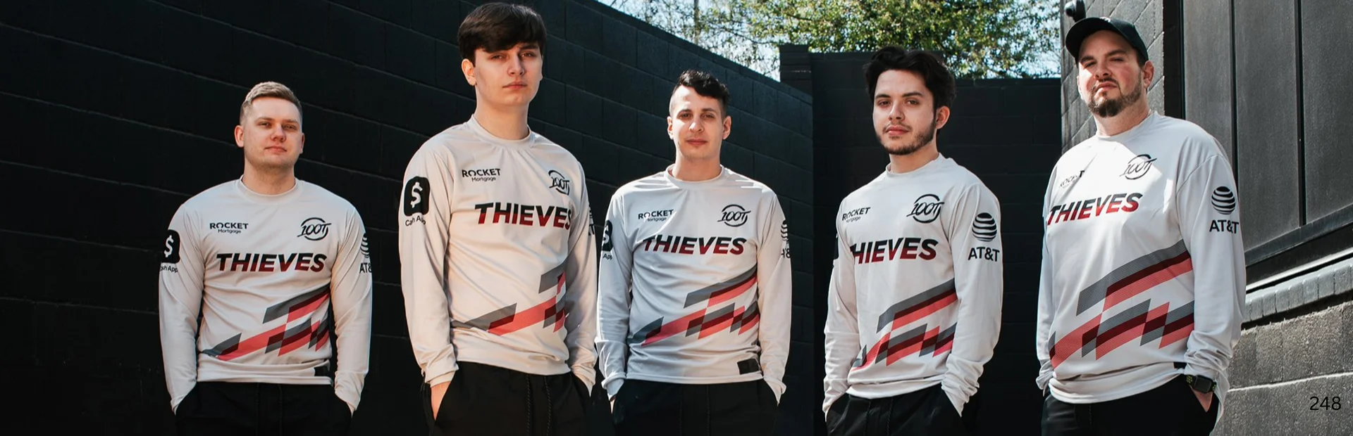 Five 100 Thieves VALORANT team members stand together outdoors wearing matching white esports jerseys.