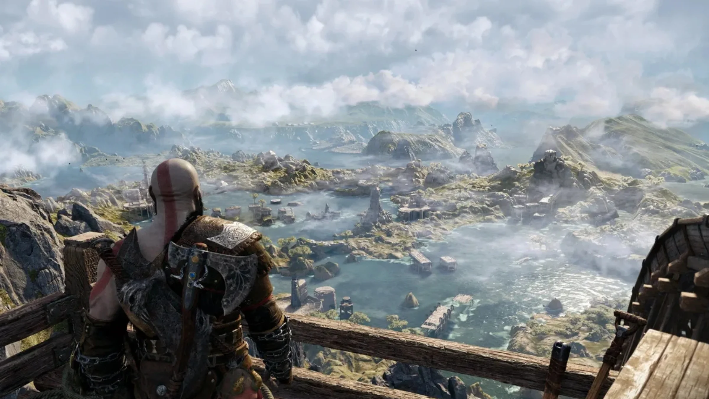 Kratos stands at a wooden overlook, looking out across a vast mist-covered fantasy landscape.