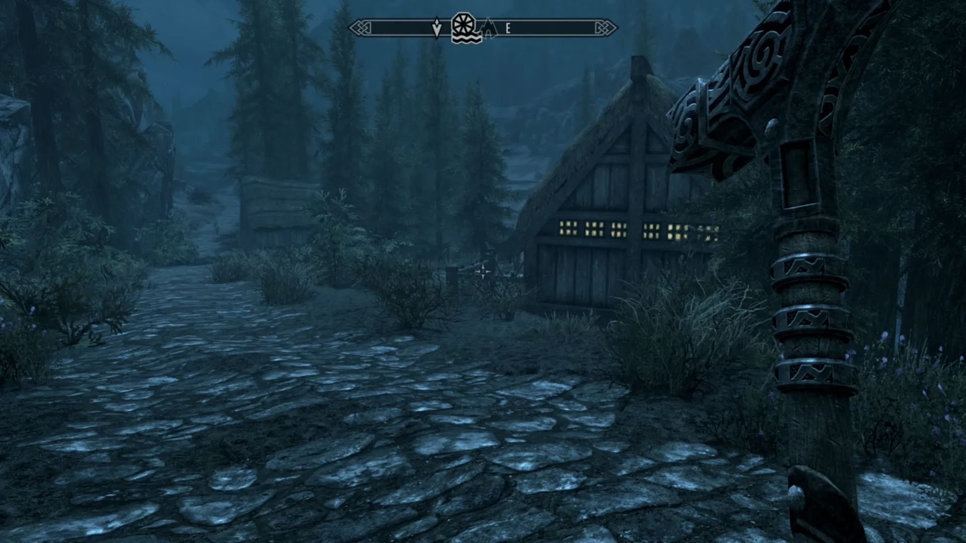 First-person view of a dark village road in Skyrim with a weapon raised.