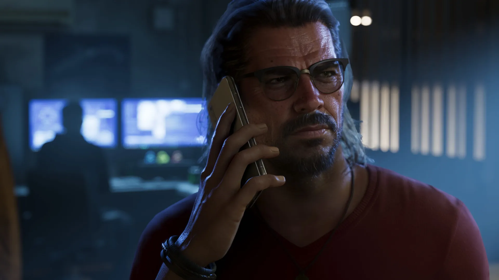 A man with glasses talks on the phone in a dark office in Grand Theft Auto VI.