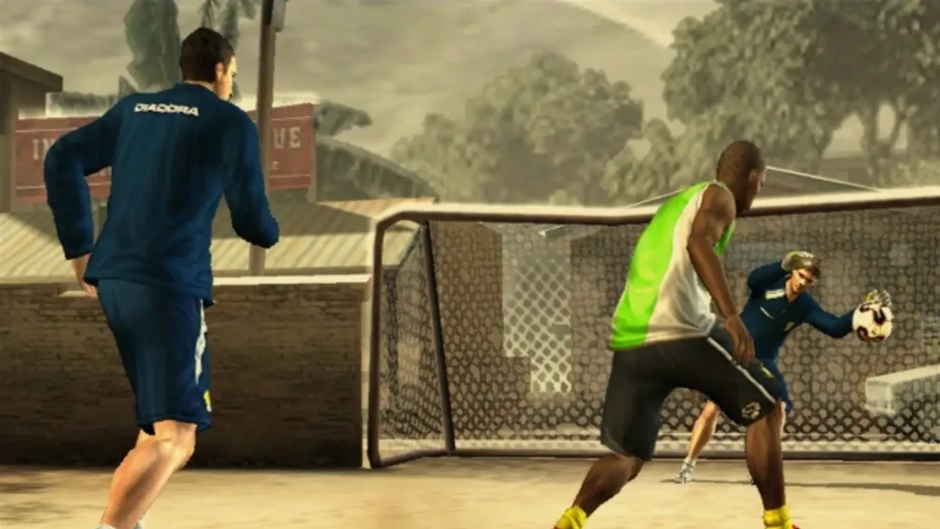 An attacker in a green vest squares up near a caged goal on a dusty outdoor pitch as the keeper holds the ball in FIFA Street 2.
