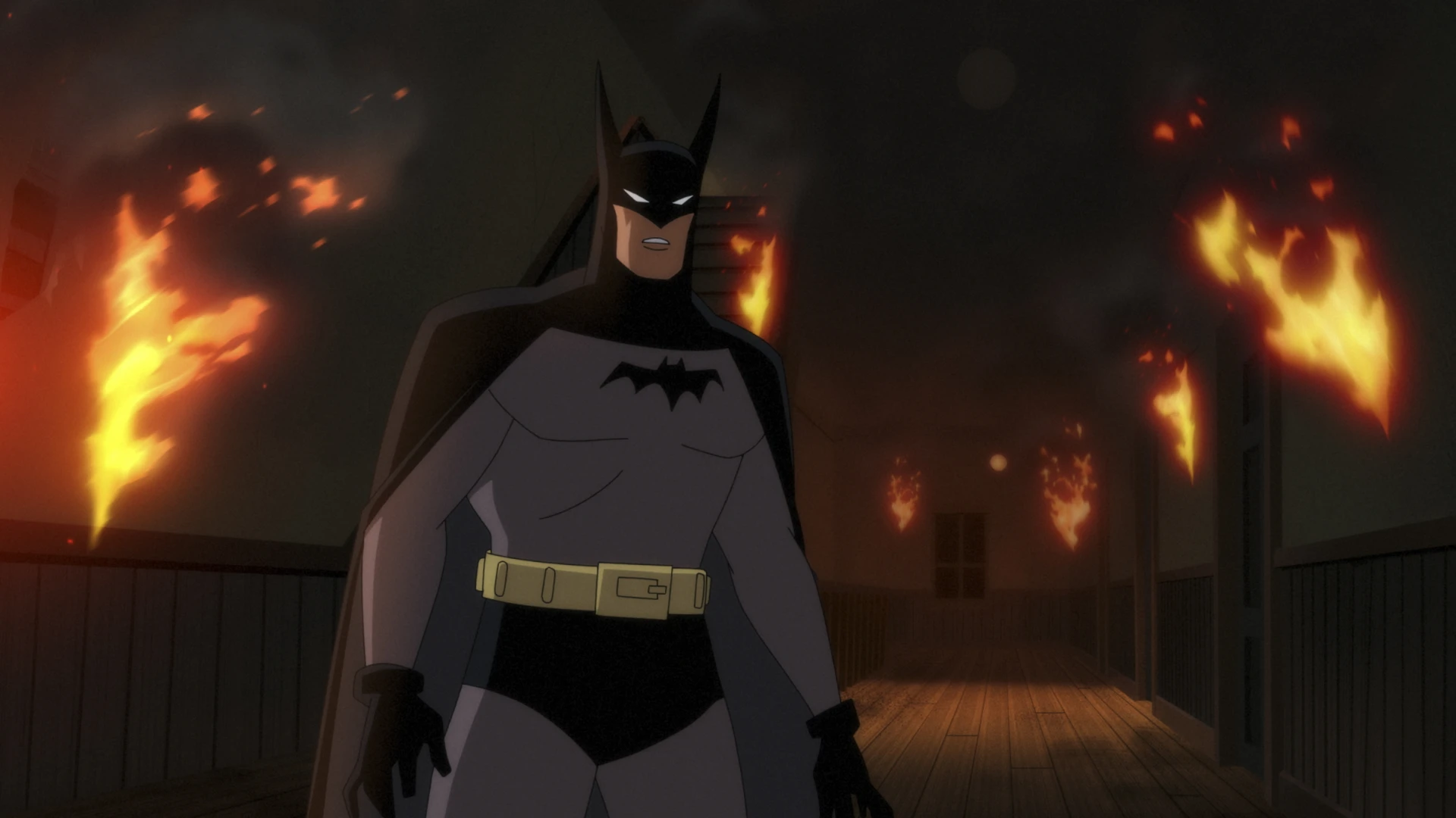 Batman standing in a dark hallway as flames burn around him