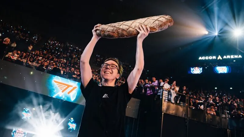 Thebausffs holding a giant baguette above his head in front of fans at a League of Legends event.
