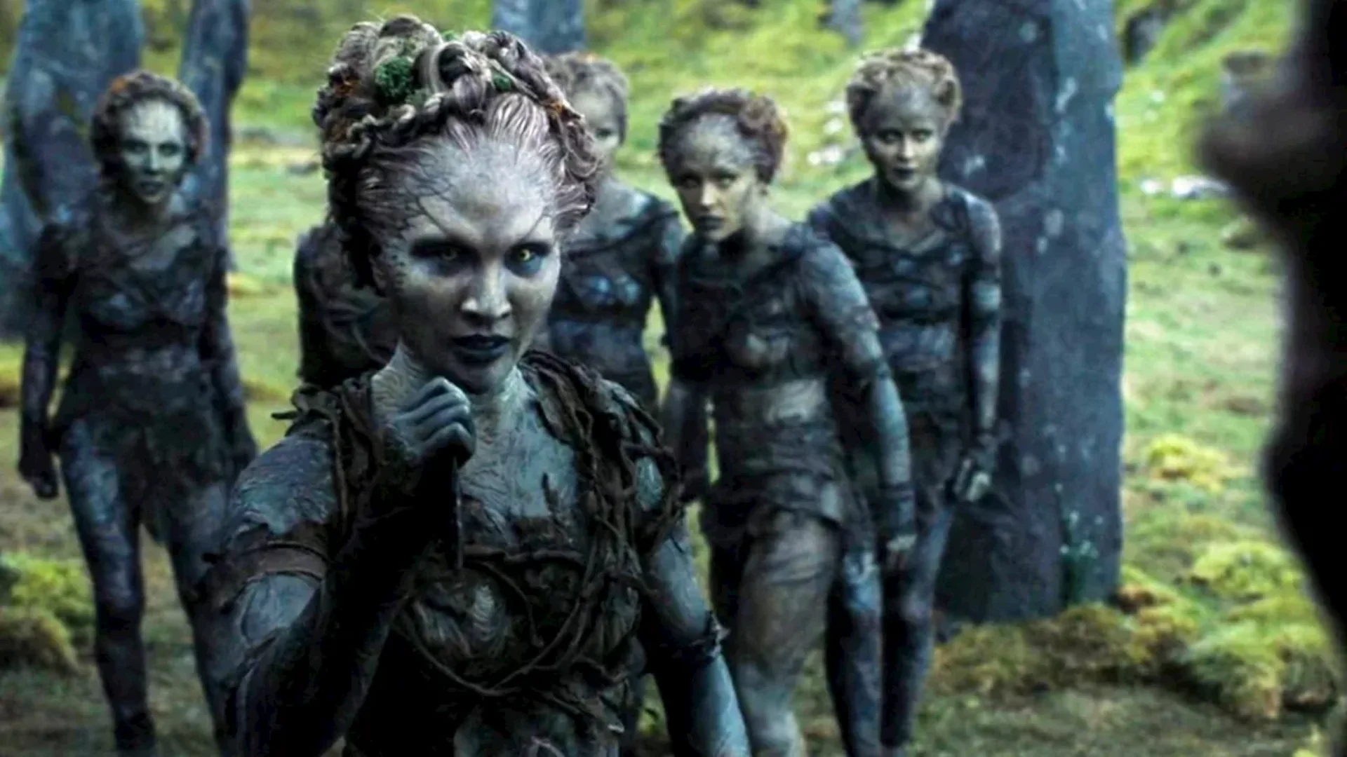 Grey-skinned forest figures gather among standing stones in a green woodland scene from Game of Thrones.