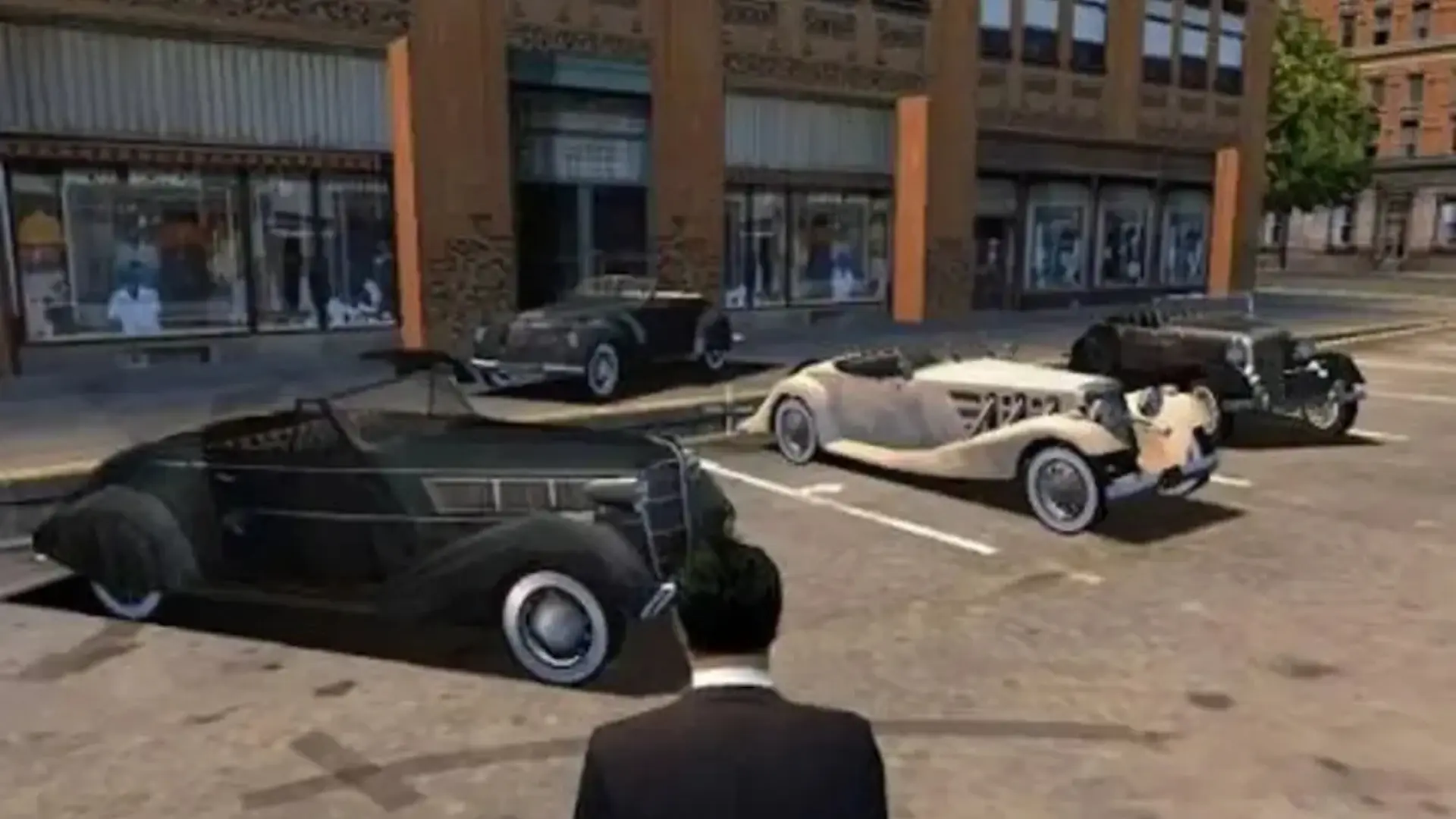 Tommy Angelo stands on a Lost Heaven street surrounded by 1930s cars in Mafia: The City of Lost Heaven.
