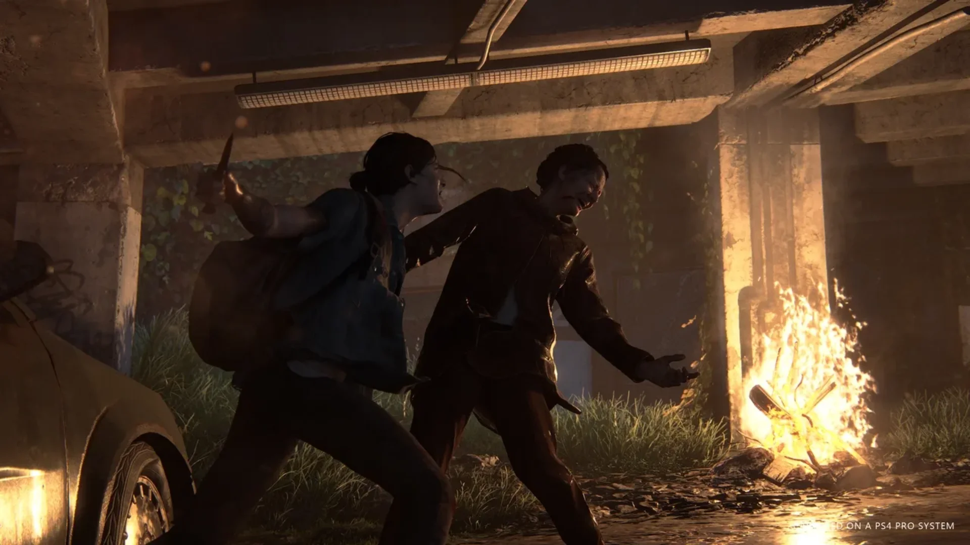 Two survivors fight beside a burning fire inside an abandoned structure in The Last of Us Part II.