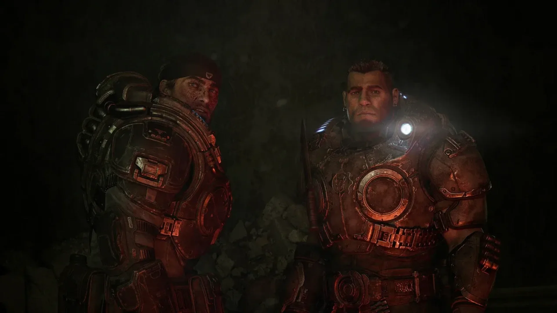 Two heavily armored Gears soldiers stand inside a dark underground area illuminated by red light.