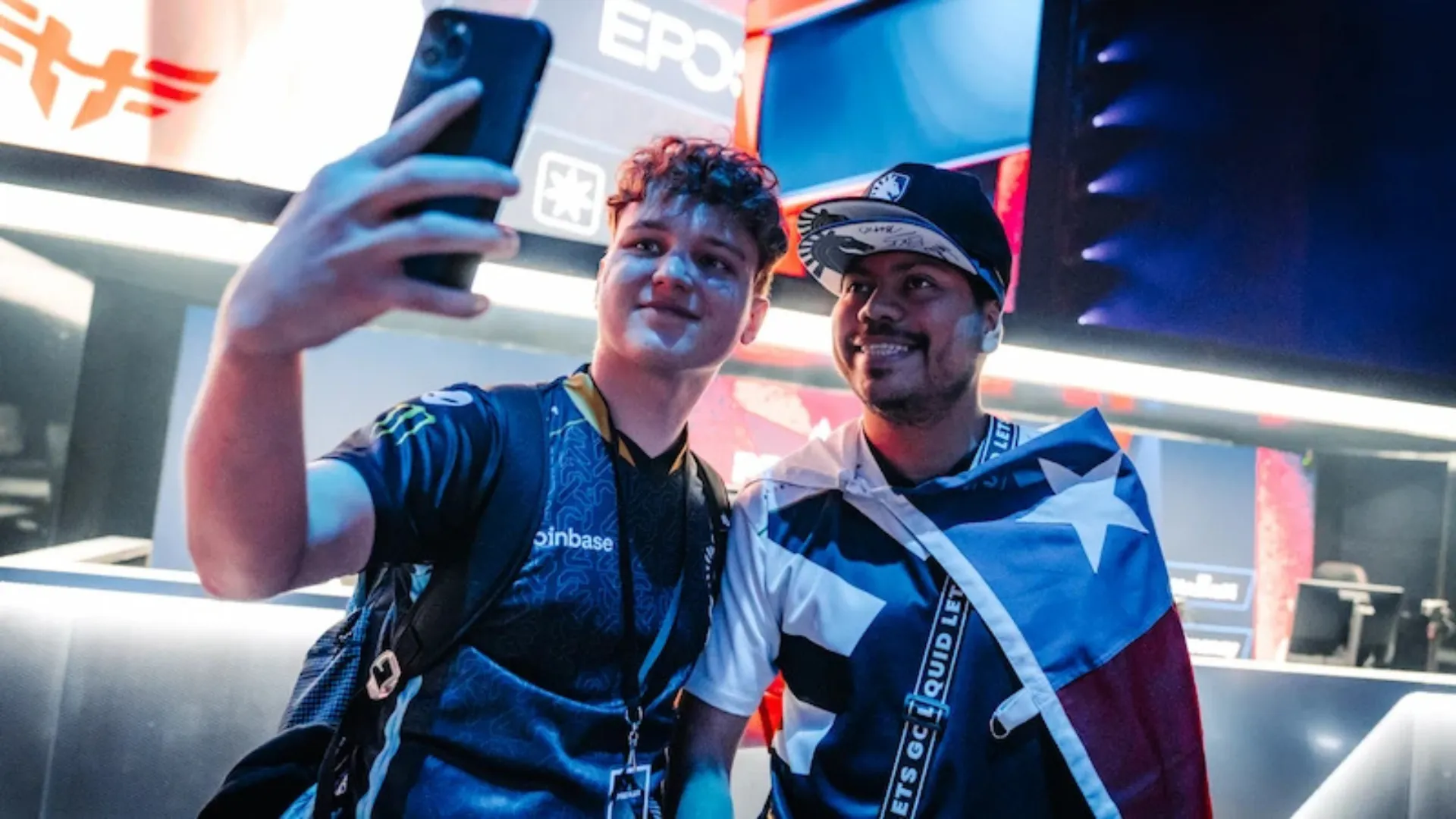 A Team Liquid player in jersey takes a selfie with a fan draped in a Team Liquid flag at an esports event.