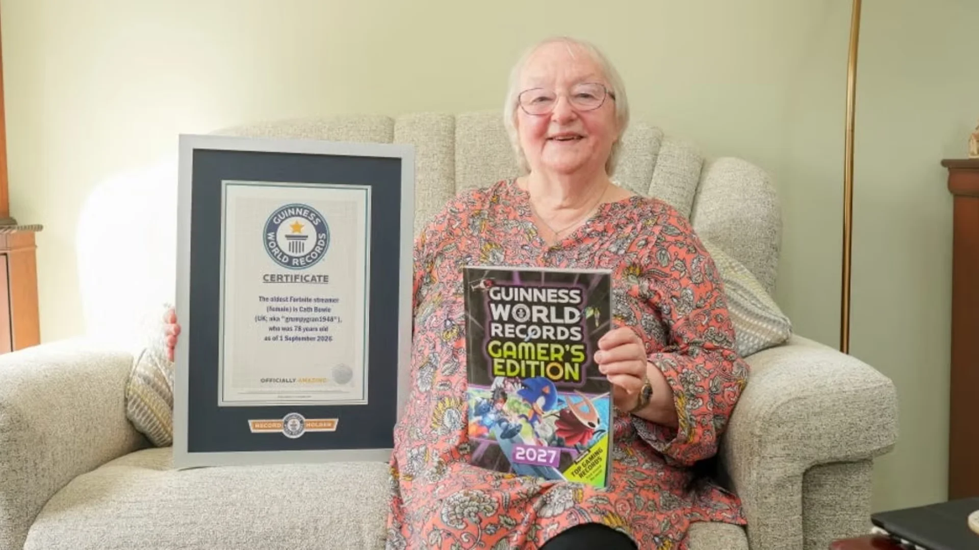 Cath Bowie holds her Guinness World Records certificate and Gamer's Edition 2027 while seated at home.