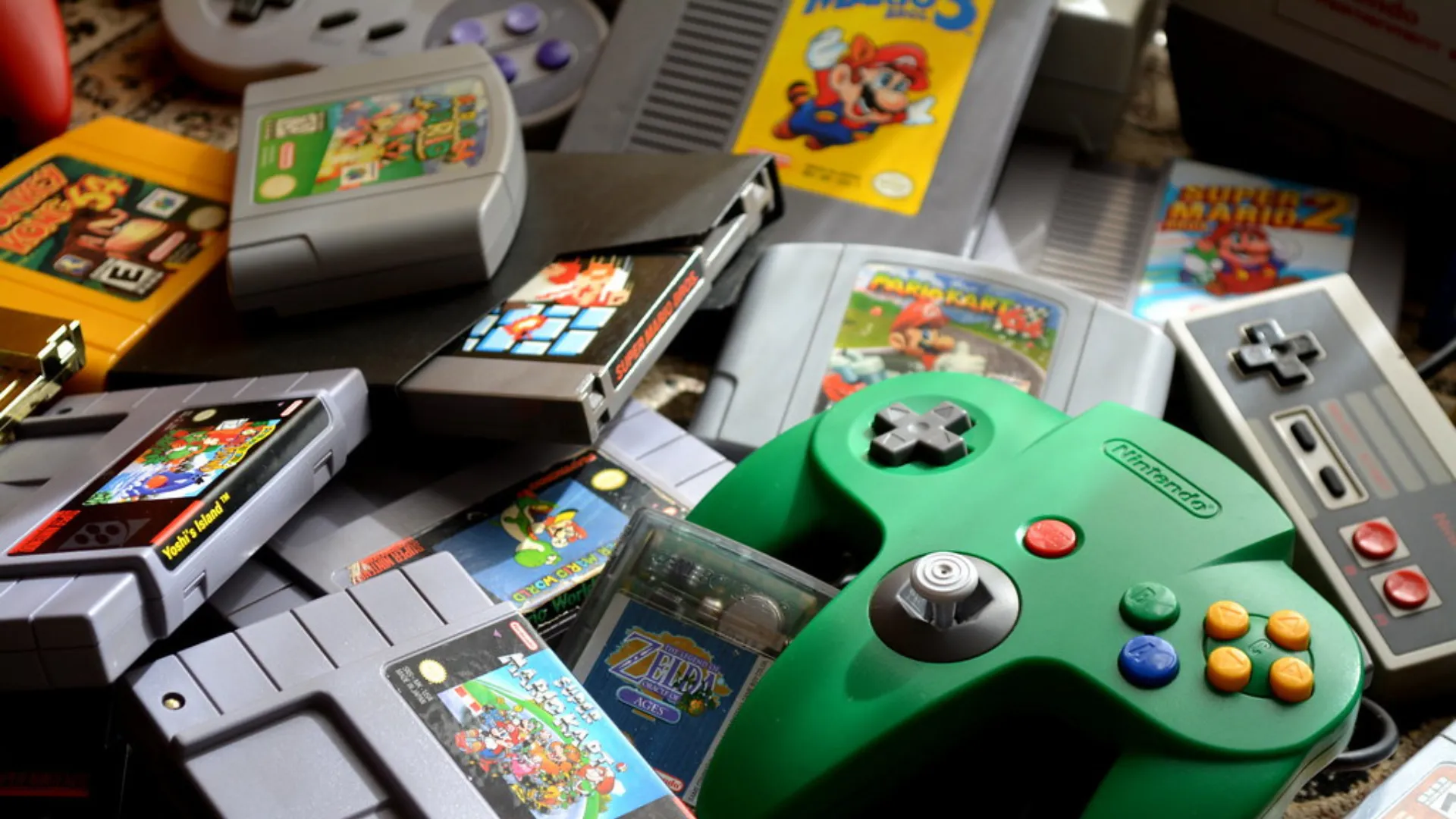 A pile of Nintendo cartridges, boxed games, an NES controller and a green Nintendo 64 controller on a carpet.