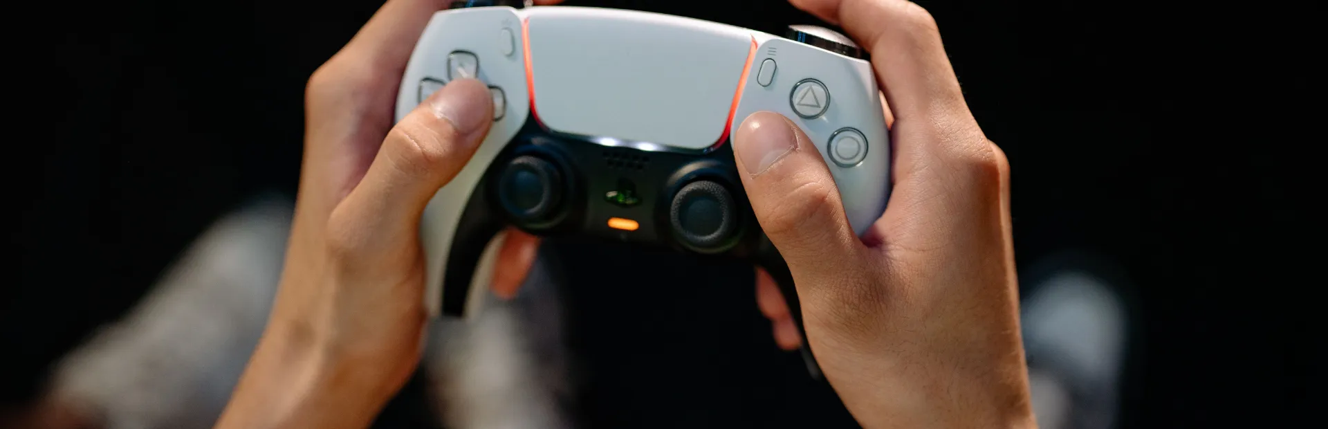 A player holds a white DualSense controller with both thumbs resting on the controls.