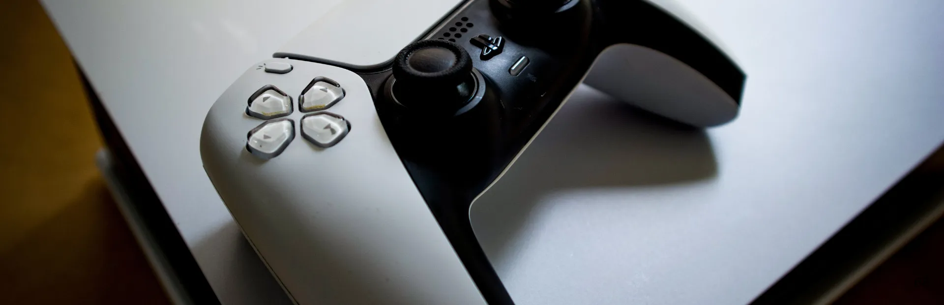 A white PlayStation 5 DualSense controller rests on top of a PS5 console.