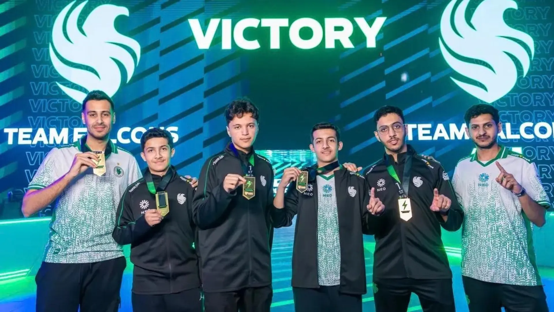 Team Falcons players and staff pose with medals in front of a victory screen