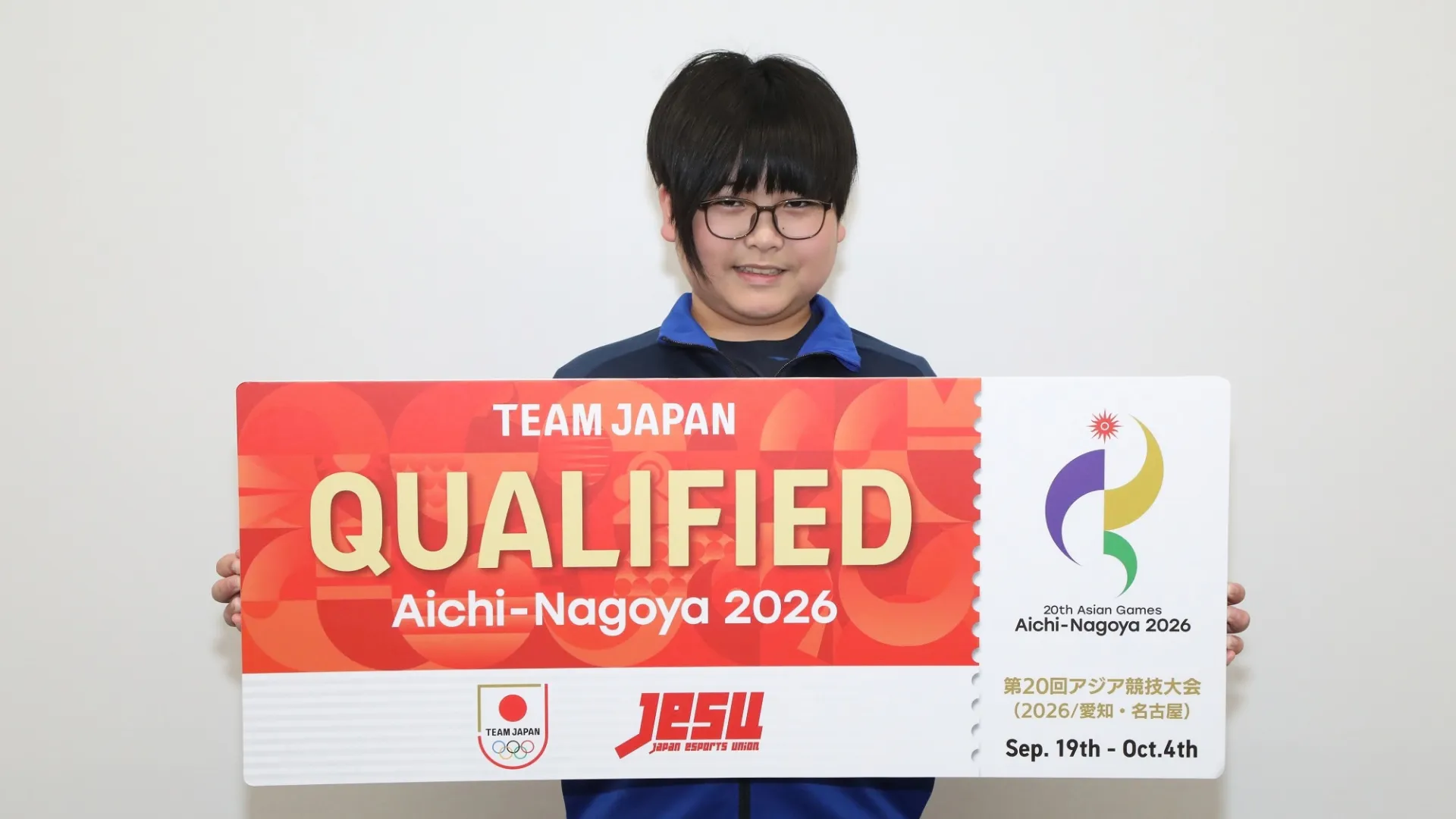 A Team Japan esports competitor holds an Aichi-Nagoya 2026 qualification sign