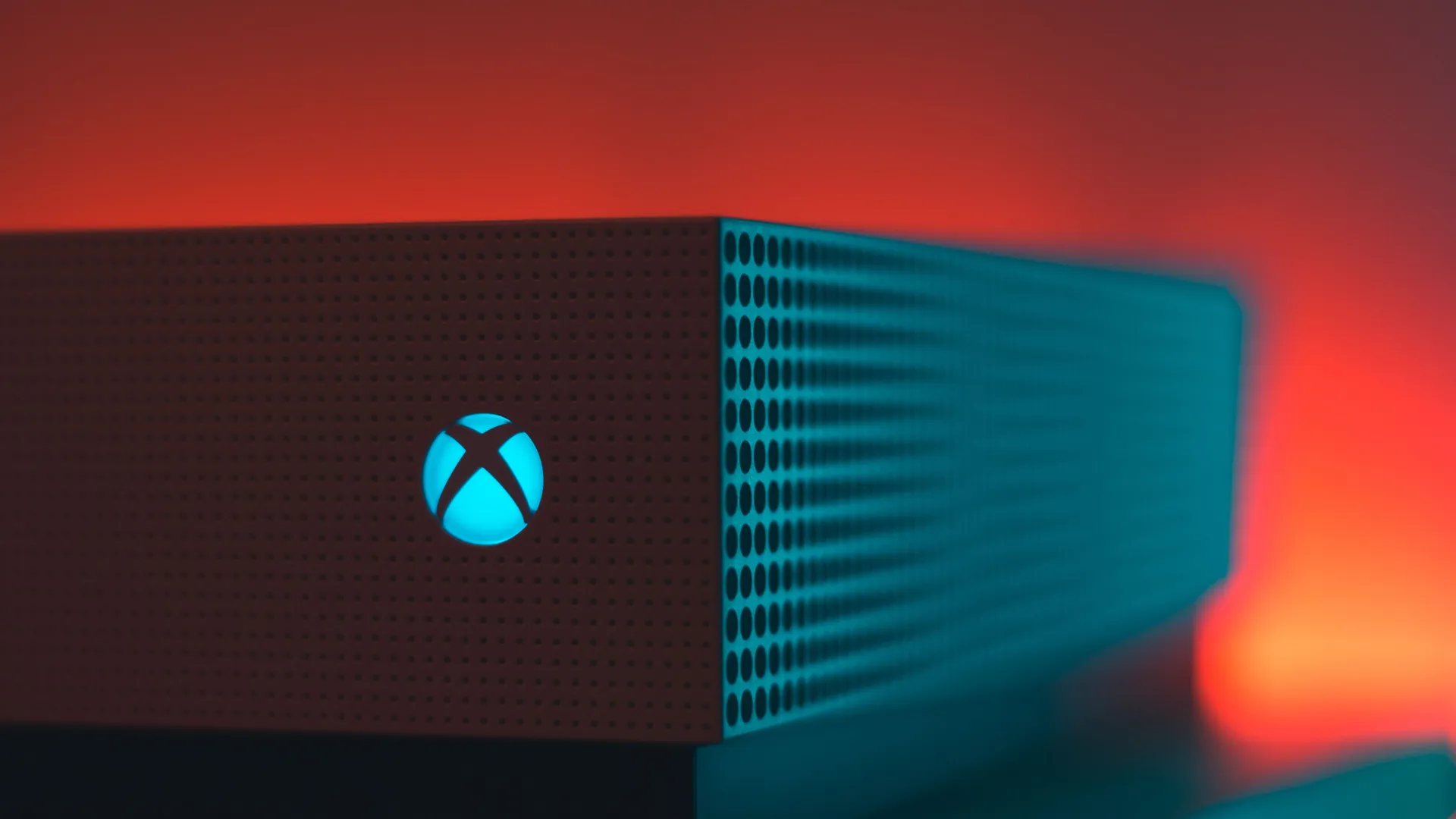 Close-up of an Xbox Series X console with its illuminated Xbox logo against red and blue lighting.