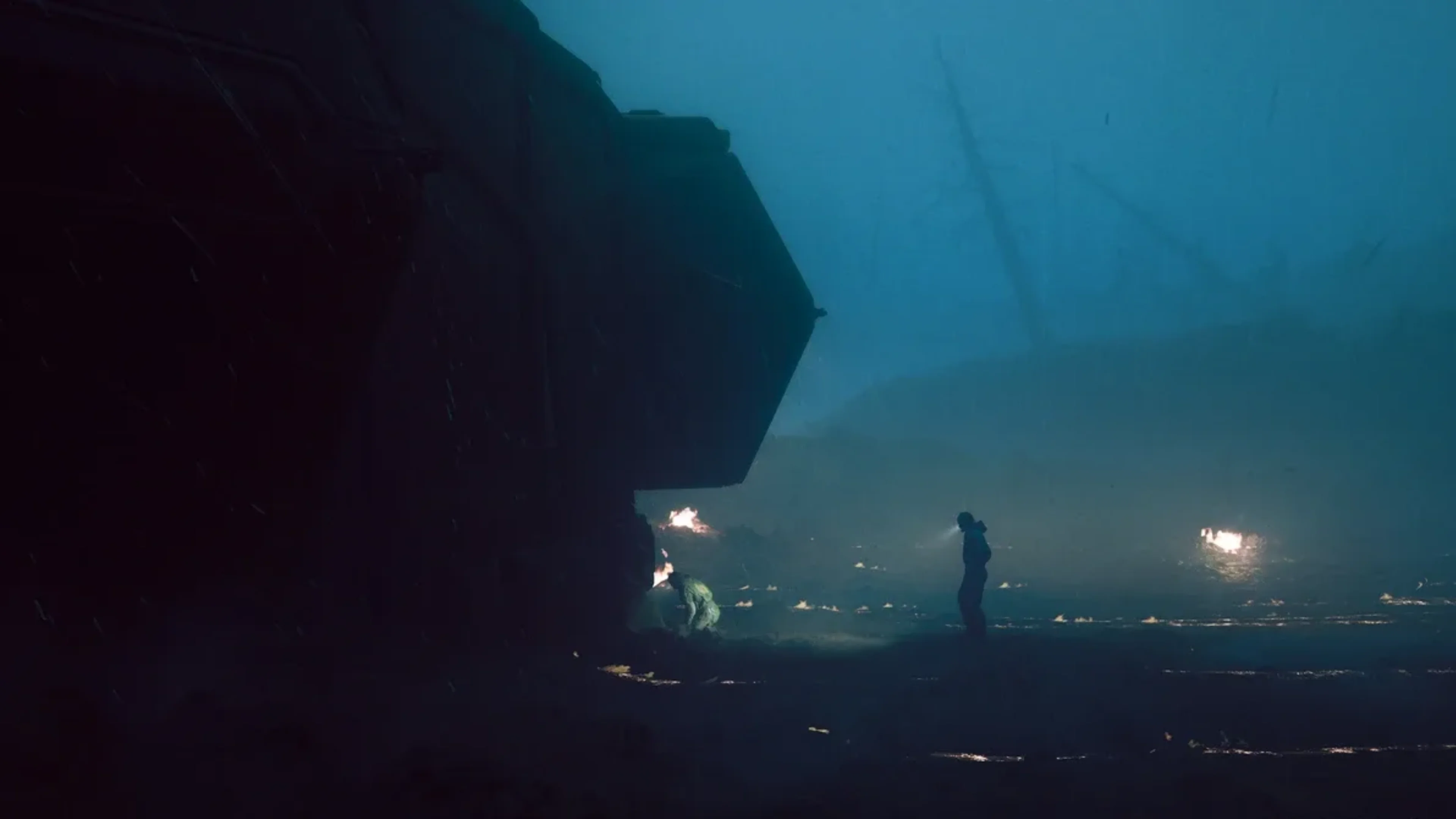 A lone figure holding a flashlight stands near a dark industrial structure in a stormy, fog-covered landscape in Alien: Isolation 2.