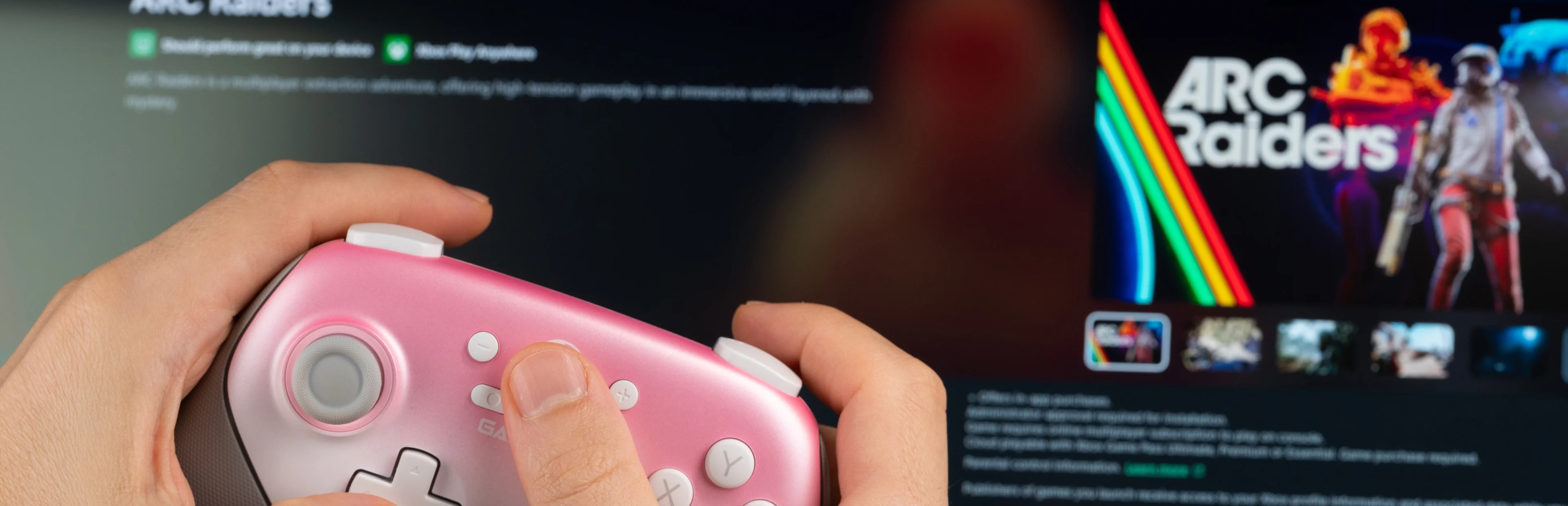 A player holds a pink game controller in front of a monitor displaying ARC Raiders artwork and game information.