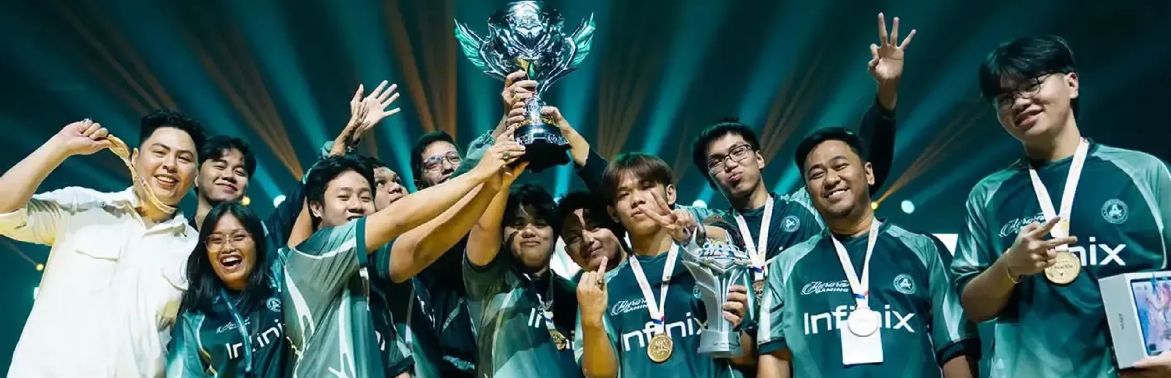 Aurora Gaming PH players and staff wearing teal Infinix jerseys celebrate together while lifting a silver esports trophy.