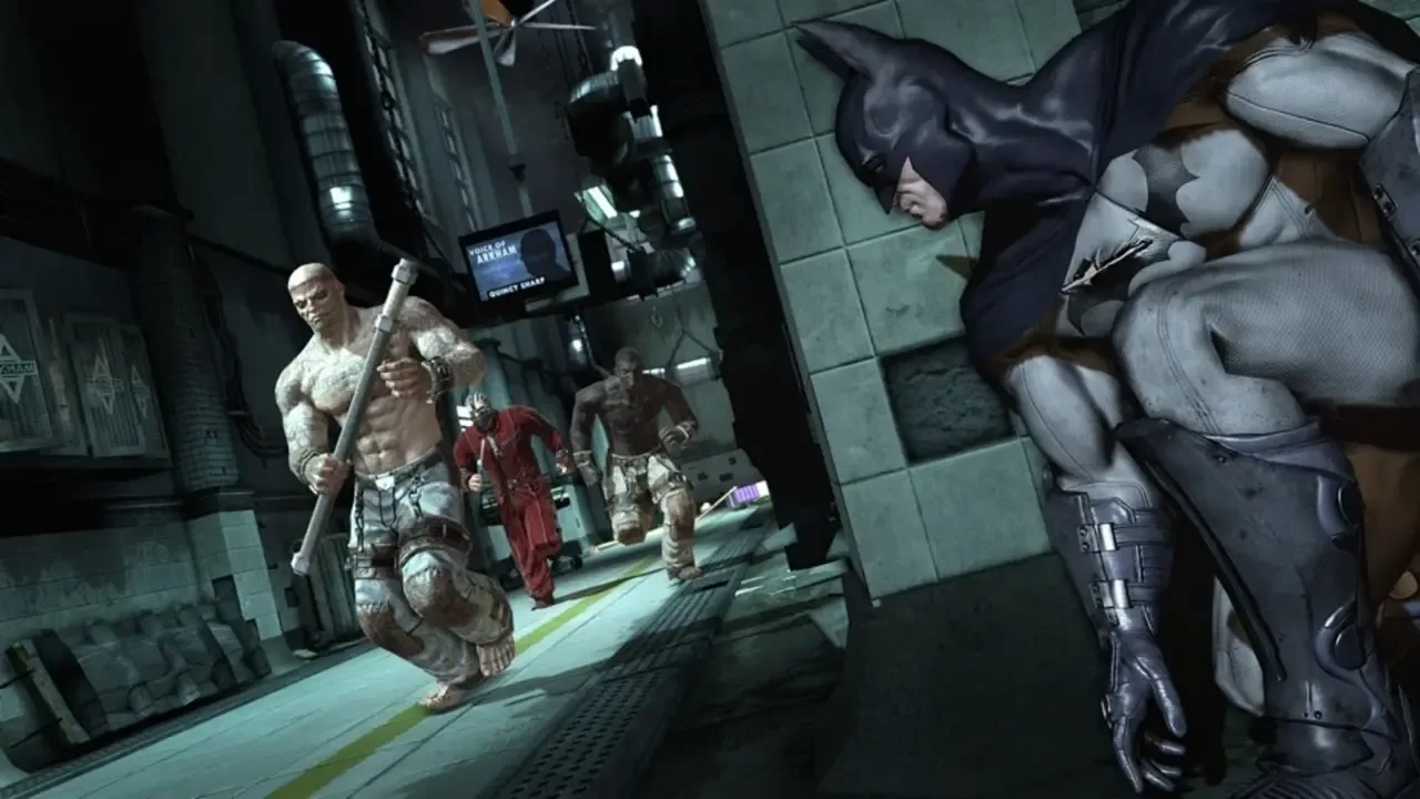Batman hides behind a wall as armed inmates run through an Arkham Asylum corridor.