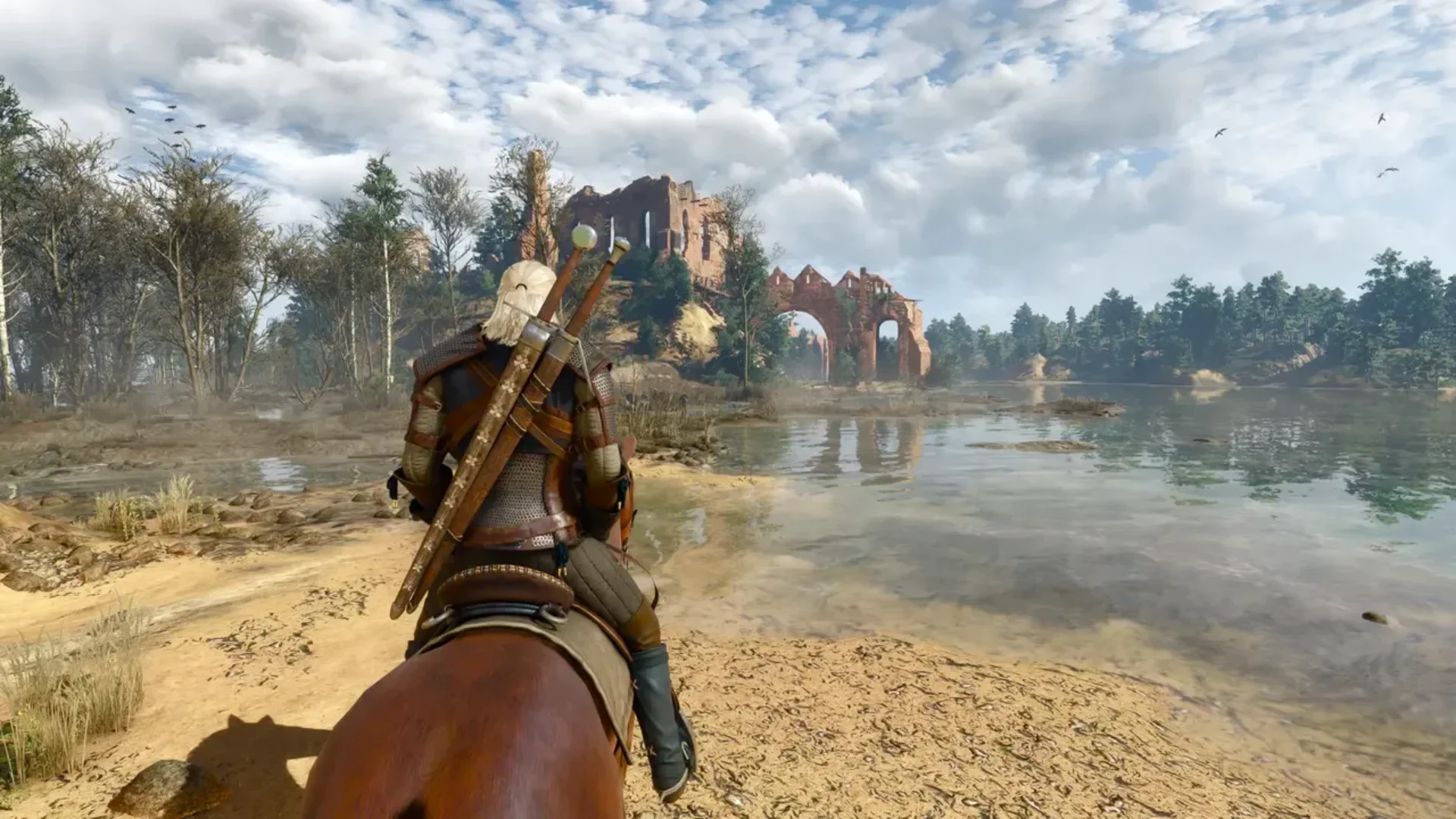 Geralt rides a horse beside a lake toward ruined stone buildings in The Witcher 3: Wild Hunt.