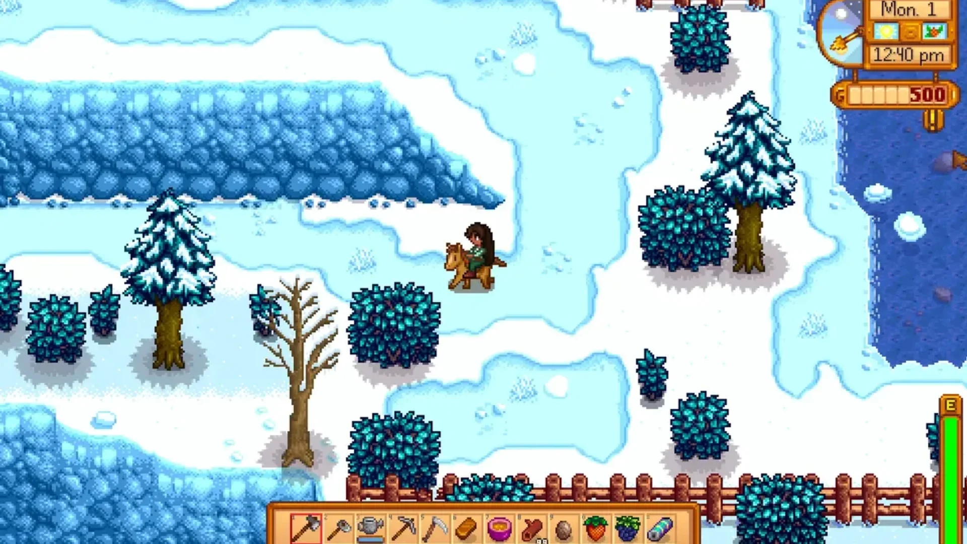 A Stardew Valley farmer rides a horse across snowy ground beside trees, bushes and a frozen river.