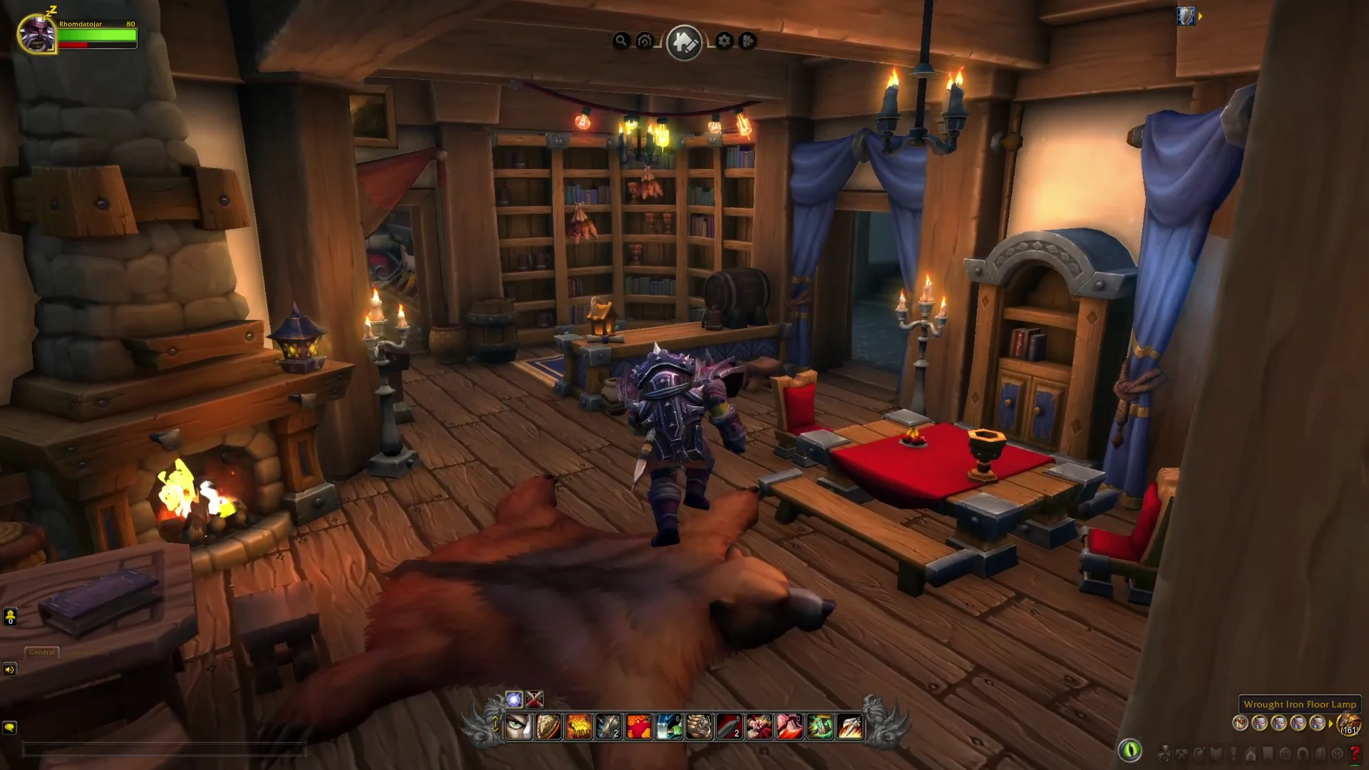 World of Warcraft player character inside a furnished wooden home with a fireplace, bookshelves, candles, and a dining table.