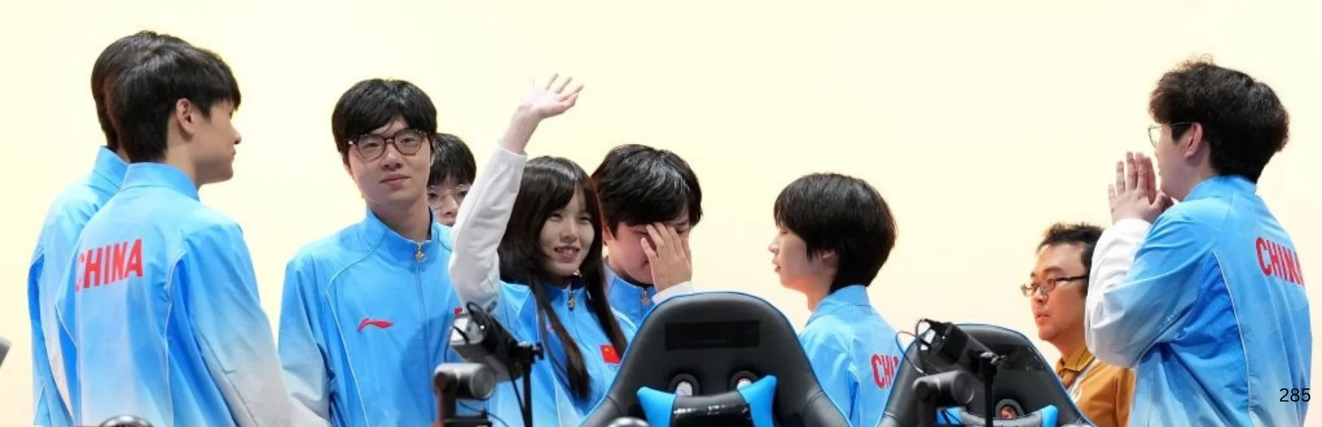 Members of China's esports team in light blue uniforms gather around gaming stations after competition.