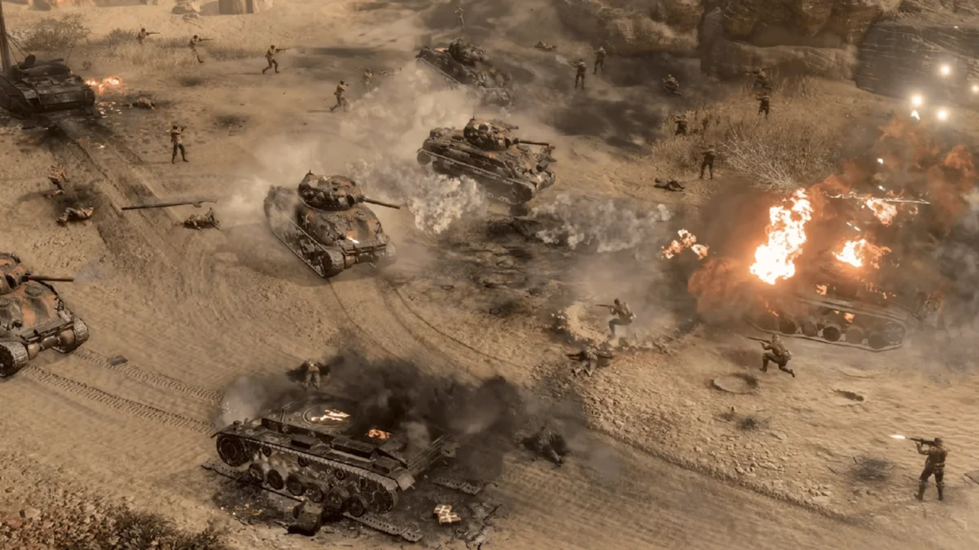 American tanks advance across a dusty World War II battlefield as infantry engage enemy forces near burning vehicles in Company of Heroes 3: Operation Torch.