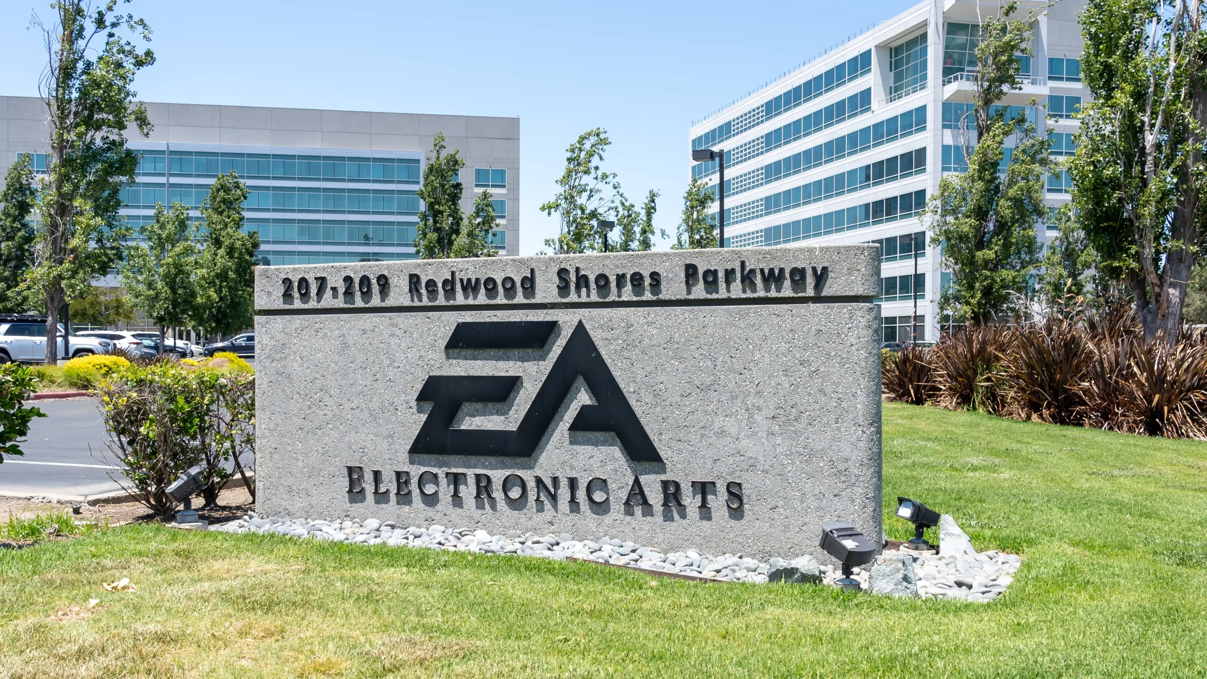 Electronic Arts headquarters sign displaying the EA logo and Redwood Shores Parkway address outside modern office buildings.