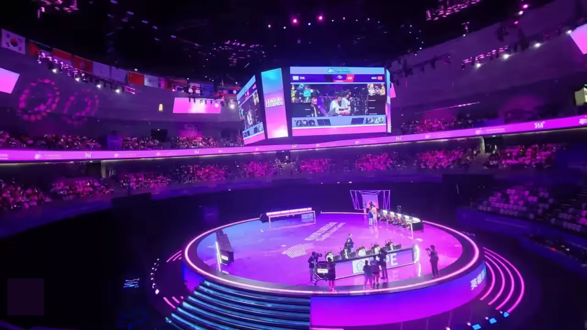 League of Legends teams compete on a circular stage inside a packed Asian Games esports arena.