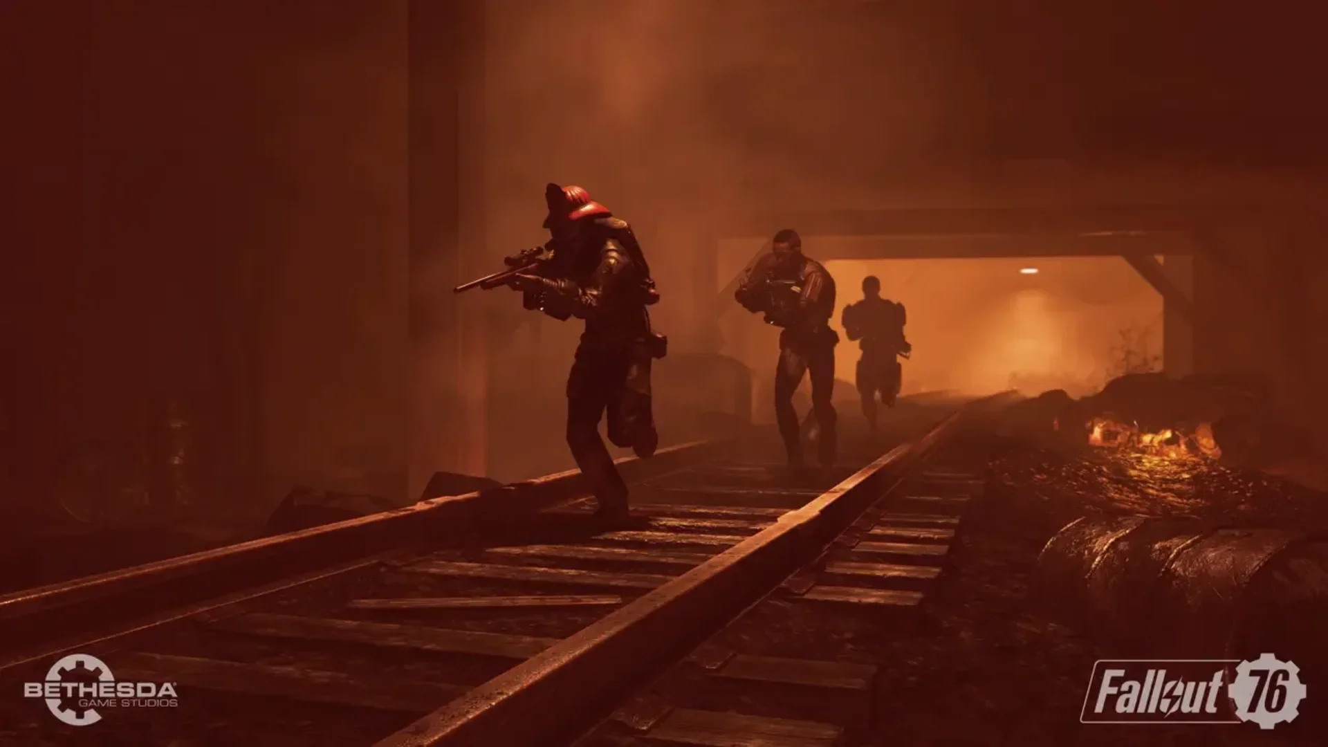 Three armed Fallout 76 characters advance along railroad tracks through an orange-lit industrial area.