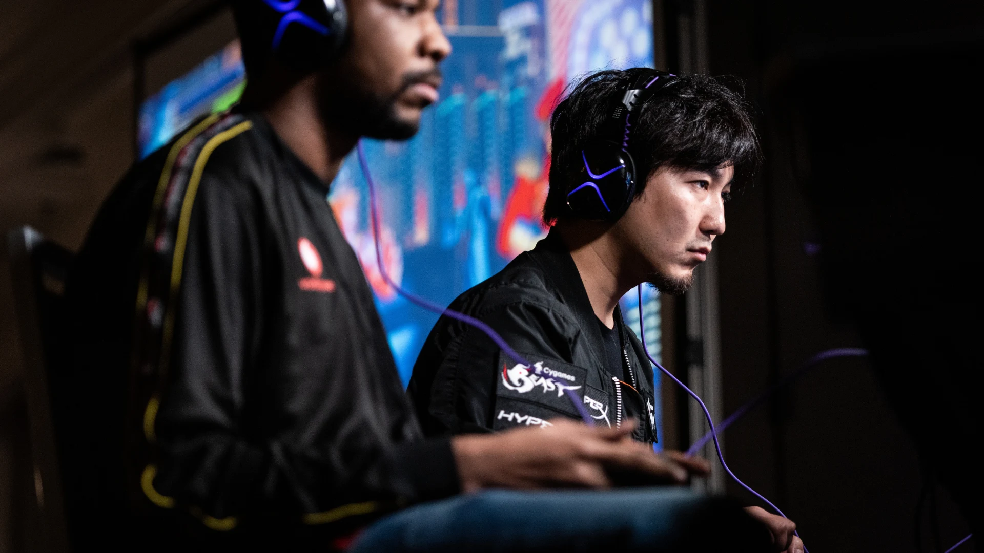 Two esports competitors wearing headsets play during a live tournament event.