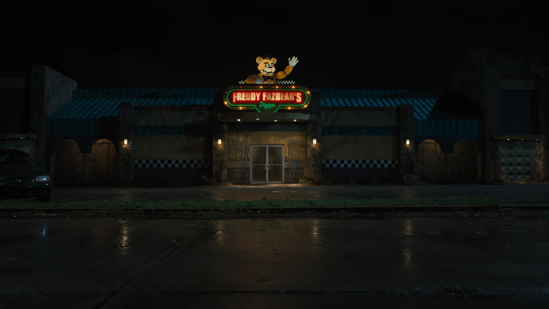 Freddy Fazbear's Pizza stands closed at night with its illuminated sign above the entrance.