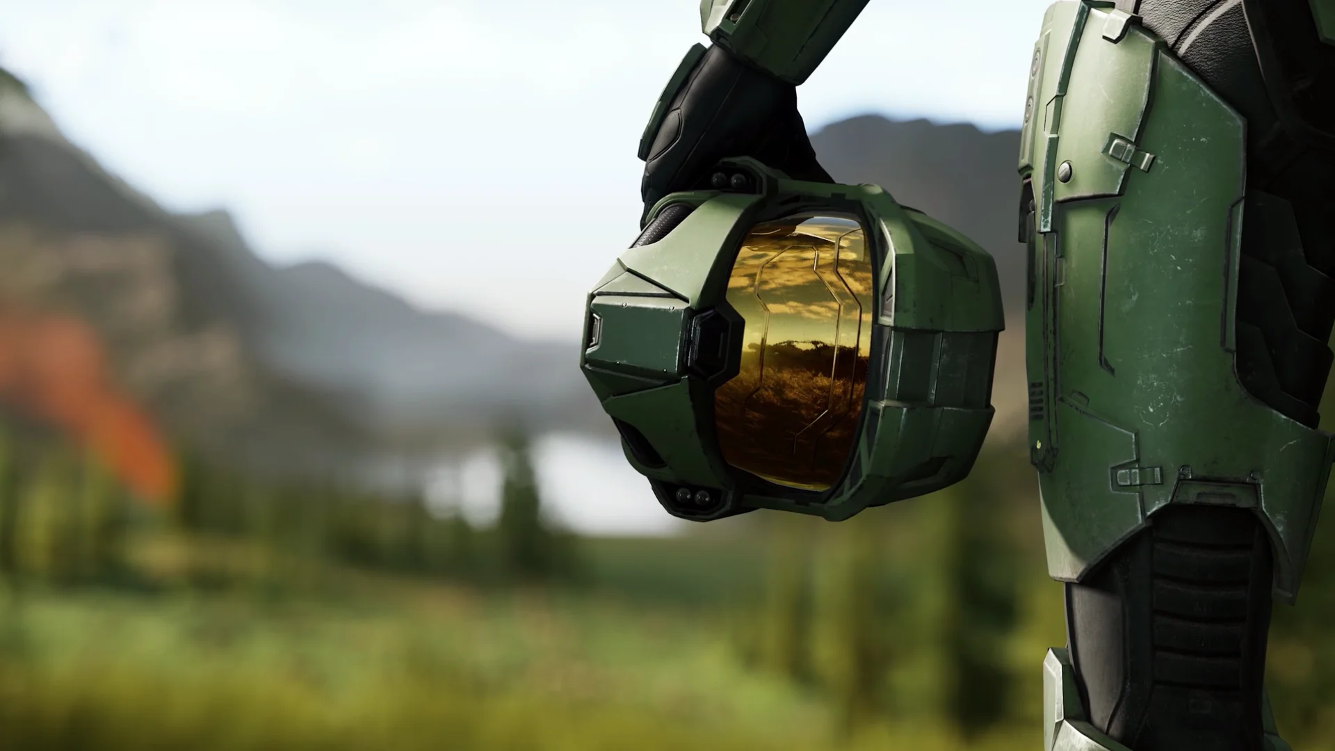Master Chief holds his green helmet at his side, with its gold visor reflecting the landscape in Halo Infinite.