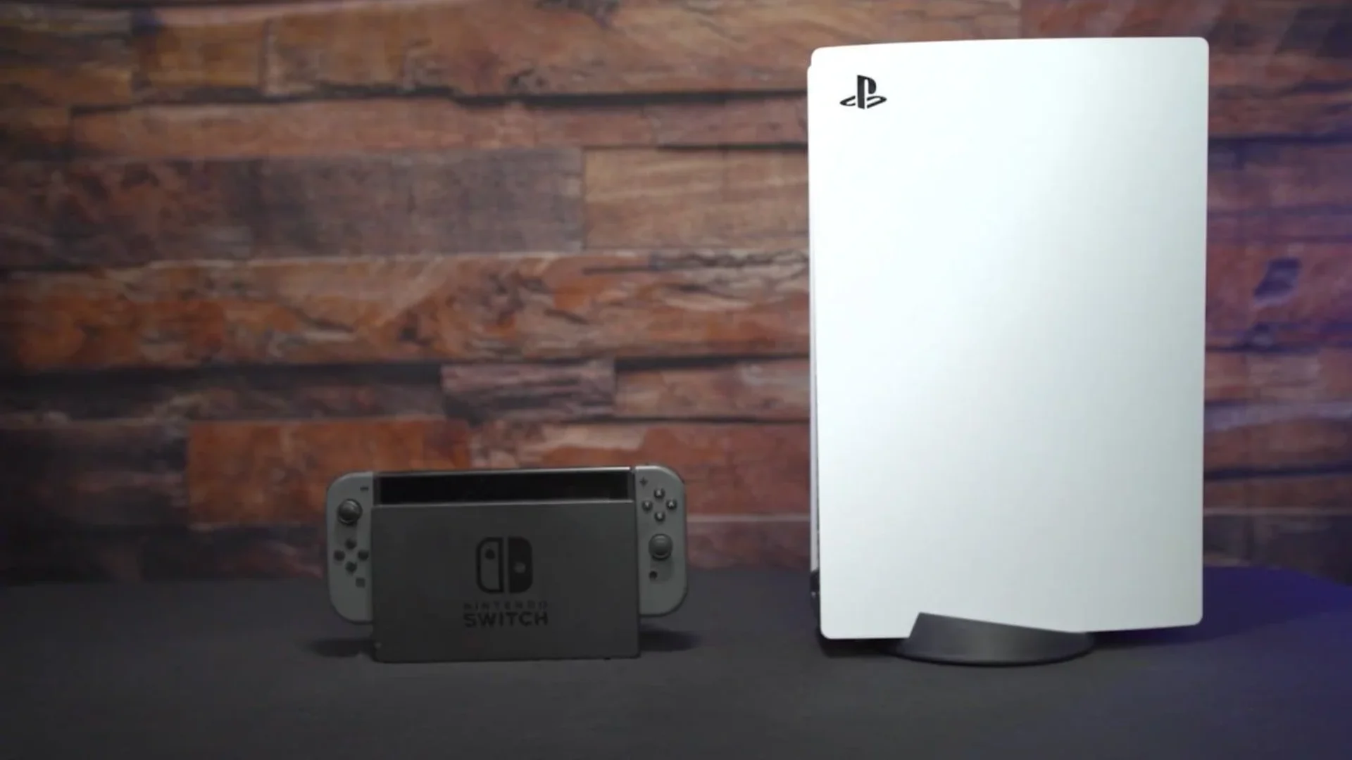 A white PlayStation 5 console stands beside a docked Nintendo Switch 2 against a wooden wall.