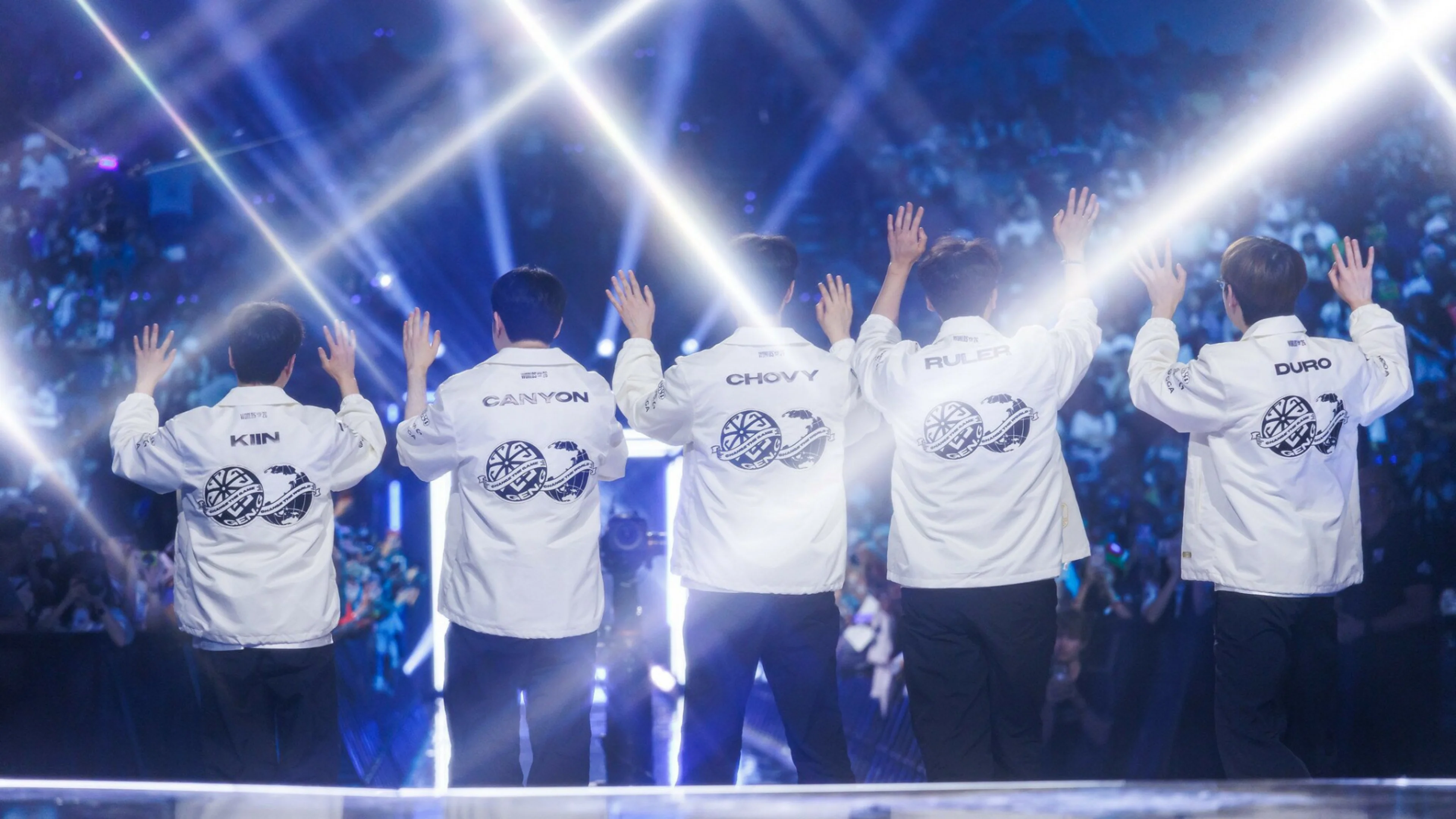 Gen.G players Kiin, Canyon, Chovy, Ruler and Duro wave to the crowd in white team jackets under bright arena lights.
