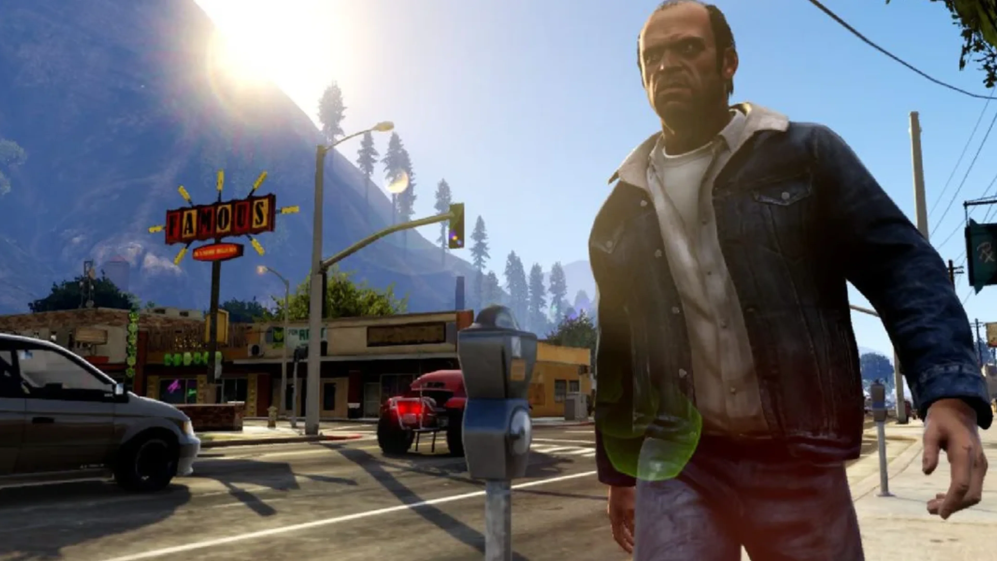 Trevor Philips walks along a sunny GTA 5 street near parked cars, storefronts and mountains in the background.