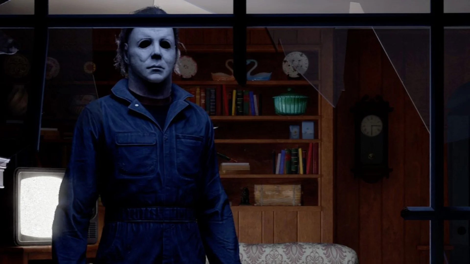 Michael Myers stands inside a dark house behind a broken window in Halloween: The Game.