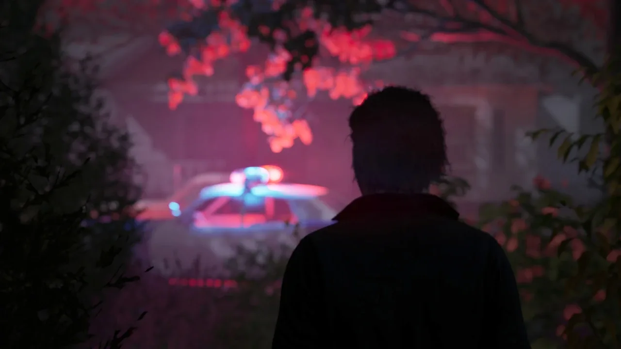 Michael Myers watches a police car with flashing red and blue lights from the shadows.