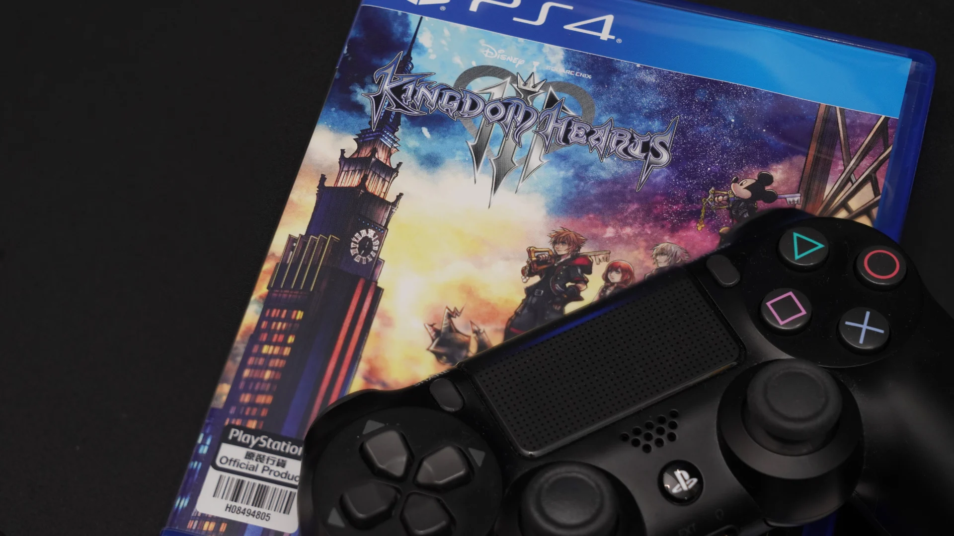 Kingdom Hearts III PS4 game case beside a black DualShock 4 controller