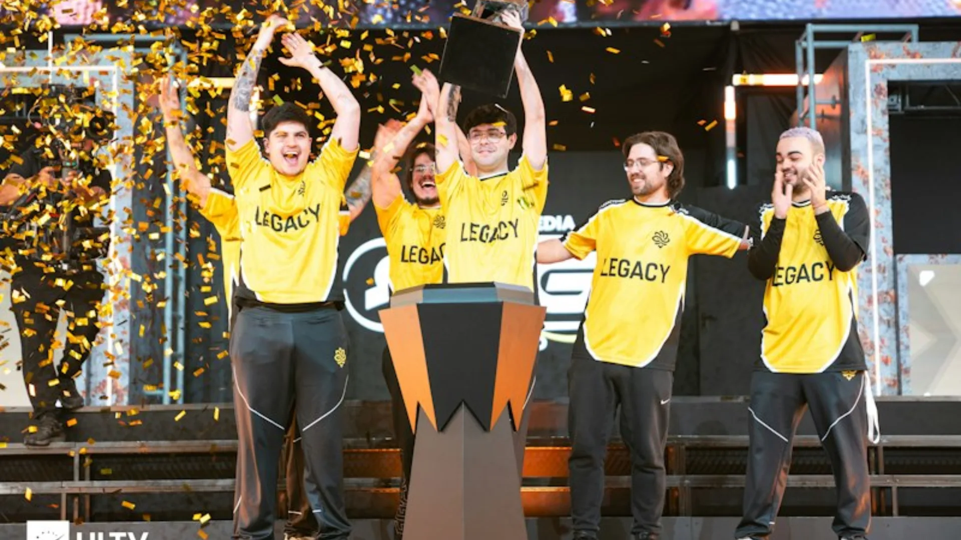Legacy Counter-Strike players celebrate on stage with a trophy and gold confetti