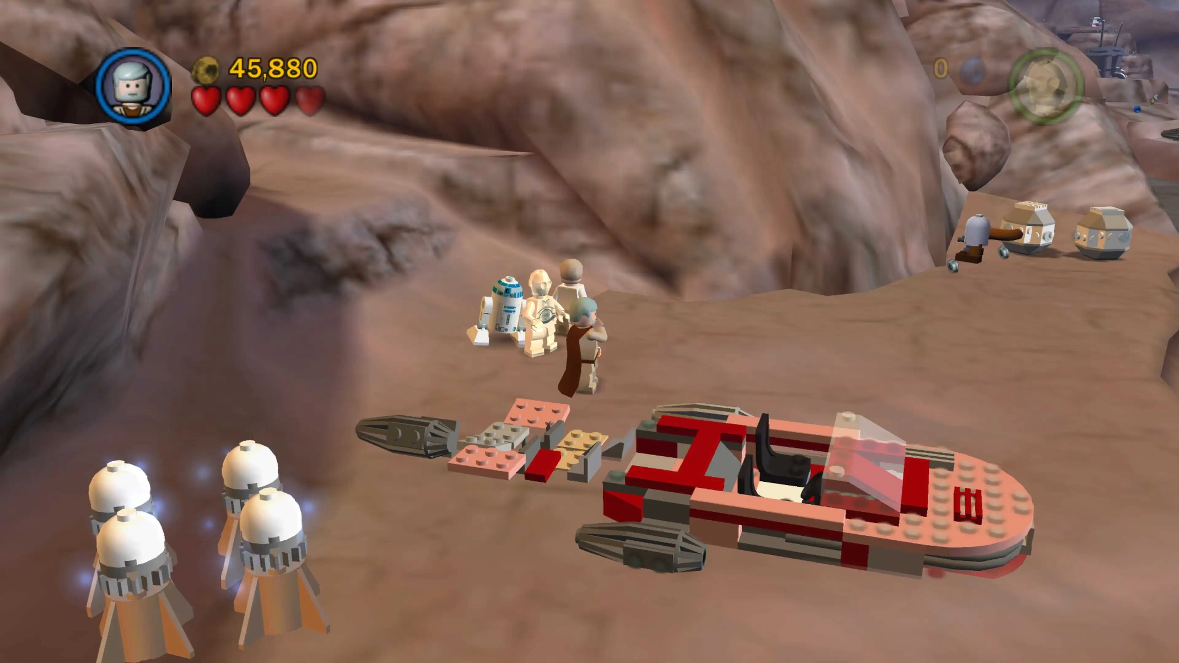 Luke Skywalker, C-3PO and R2-D2 stand beside a red-and-white landspeeder in a rocky Tatooine canyon.