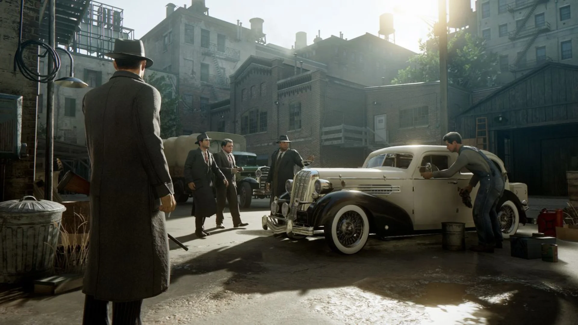 Mafia Definitive Edition gameplay showing suited characters gathered around a vintage car in a city courtyard.
