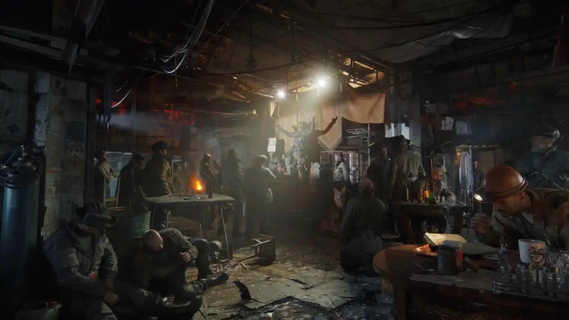Survivors gather around tables inside a dim underground Metro settlement lit by lamps and fires.