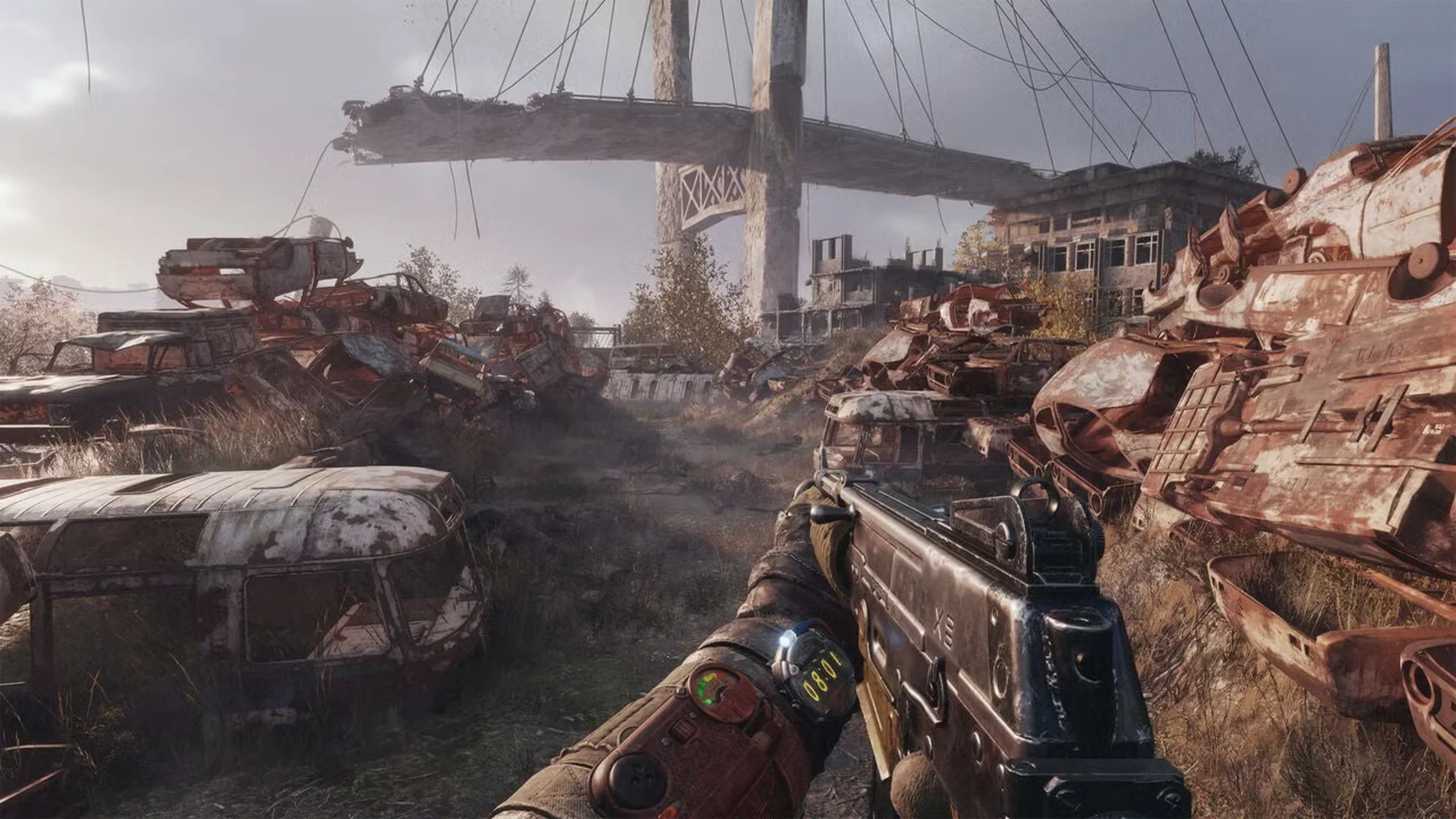 First-person Metro gameplay shows a rifle aimed through a ruined vehicle yard beneath a damaged bridge.