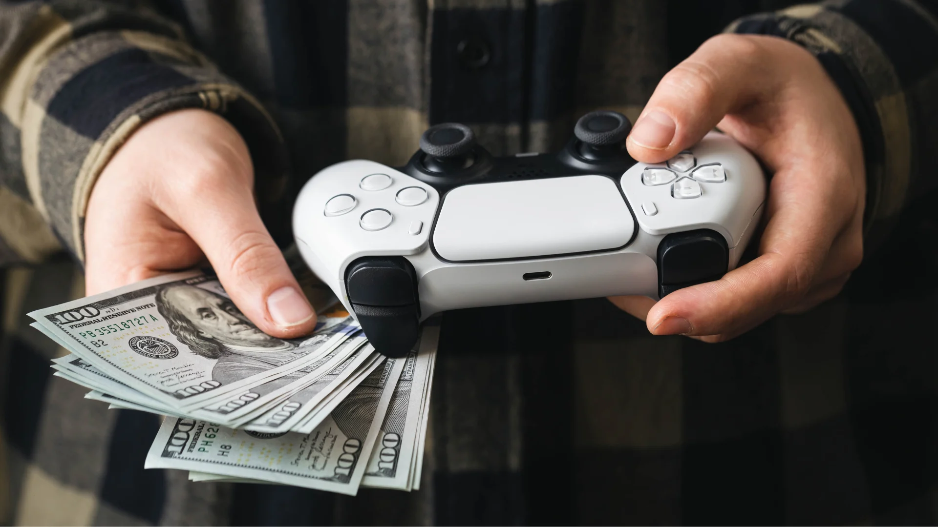 Person holding a game controller and a stack of US dollar bills