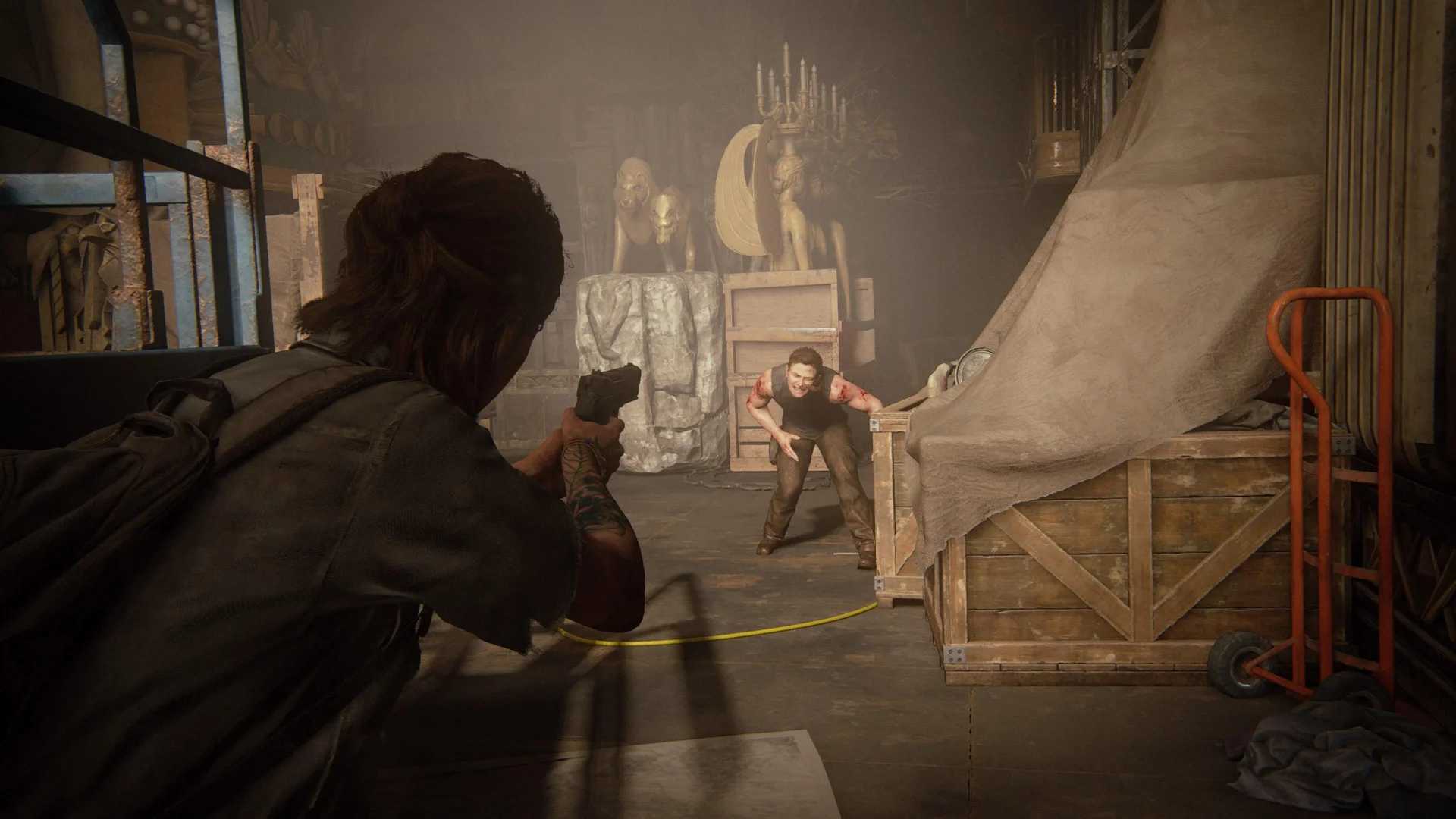 Ellie aims a handgun at an injured woman inside a cluttered interior in The Last of Us Part II.