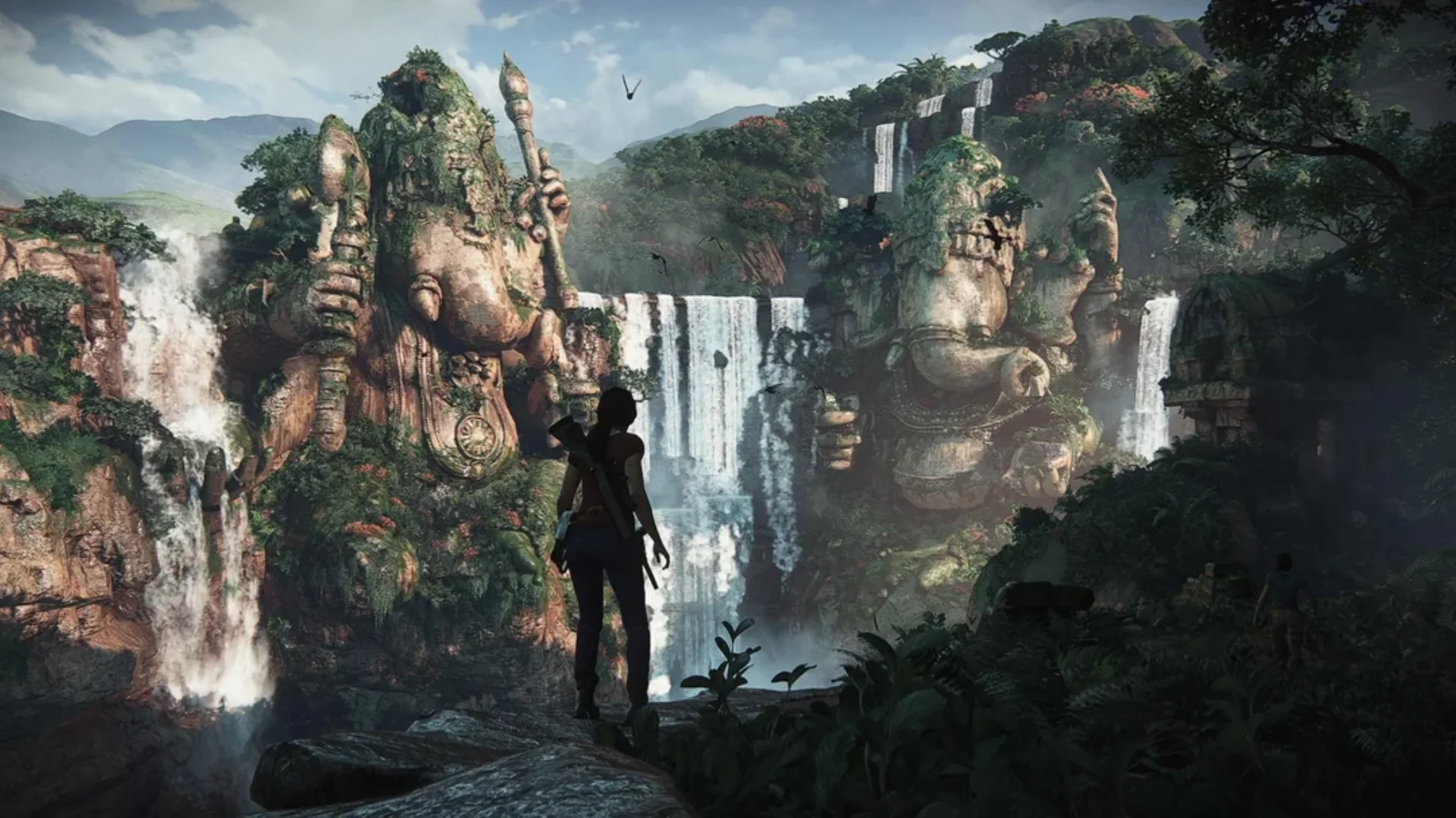 Chloe Frazer overlooks giant Ganesha statues and waterfalls in a jungle valley in Uncharted: The Lost Legacy.